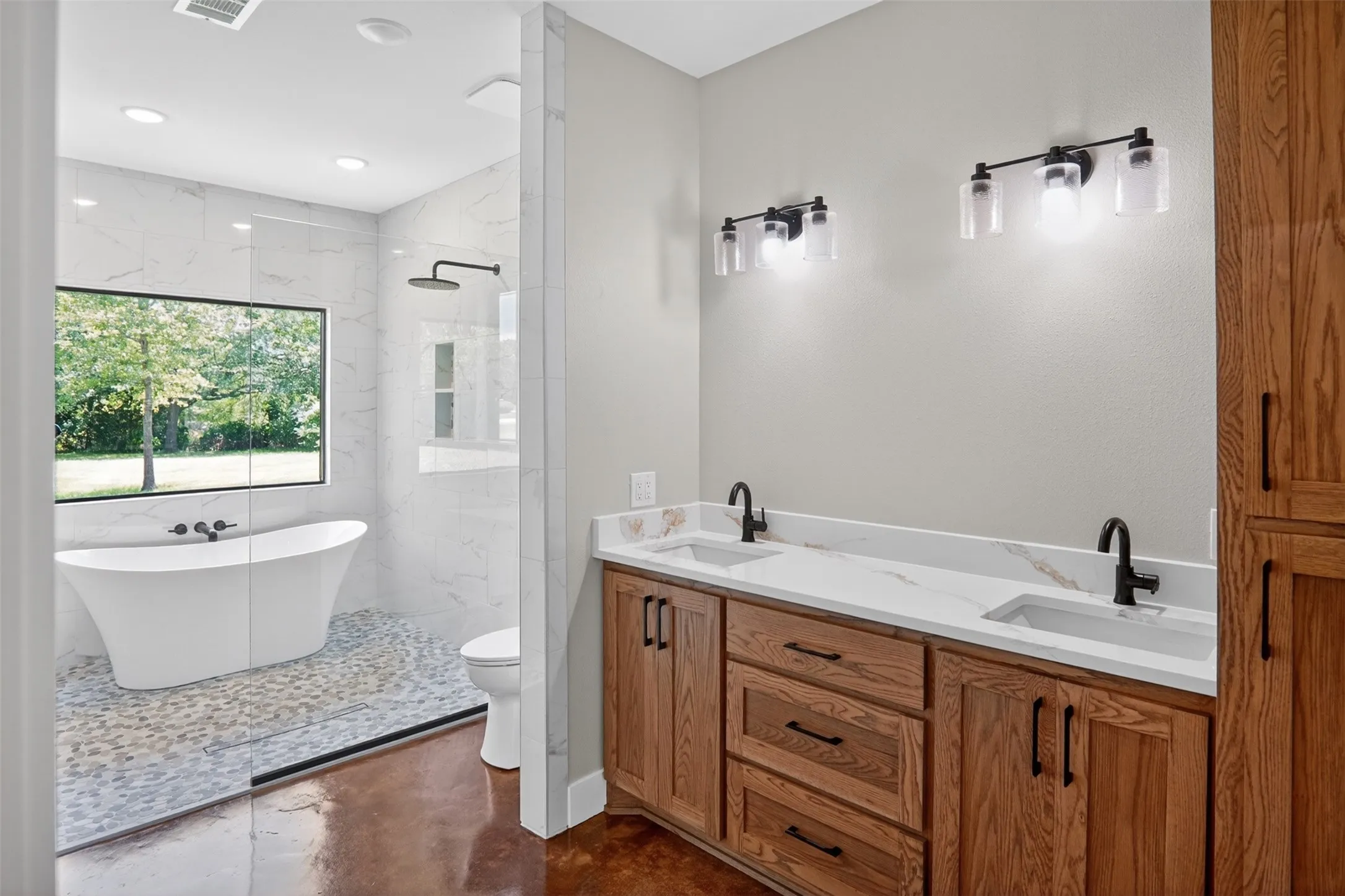 Primary Spacious bathroom featuring a dual vanity with wood cabinetry and light-toned countertops, matte black fixtures, an expansive freestanding tub, and a separate walk-in shower with pebble flooring
