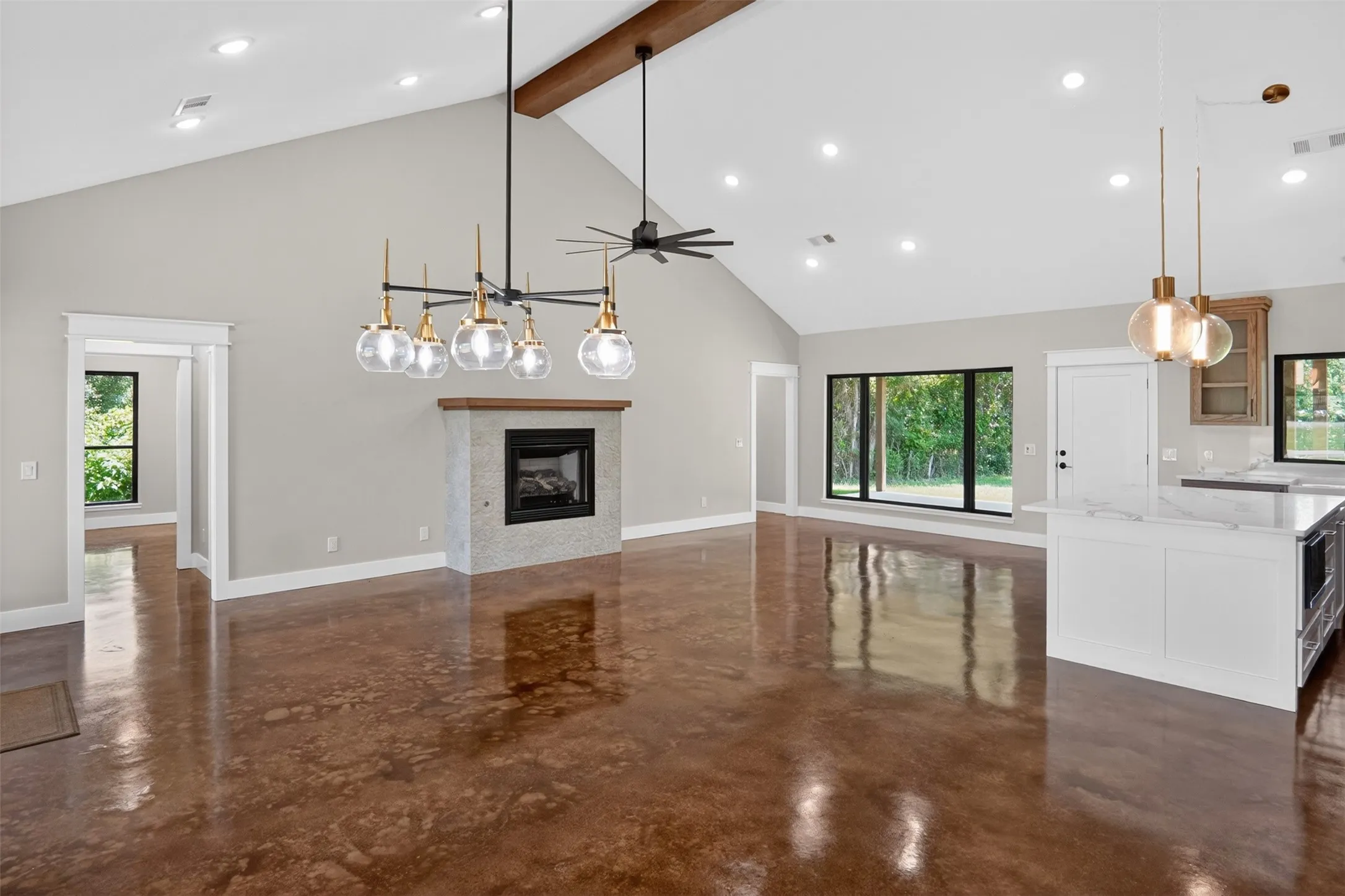 Expansive living area featuring vaulted ceilings with an exposed wood beam, recessed lighting, and polished concrete flooring