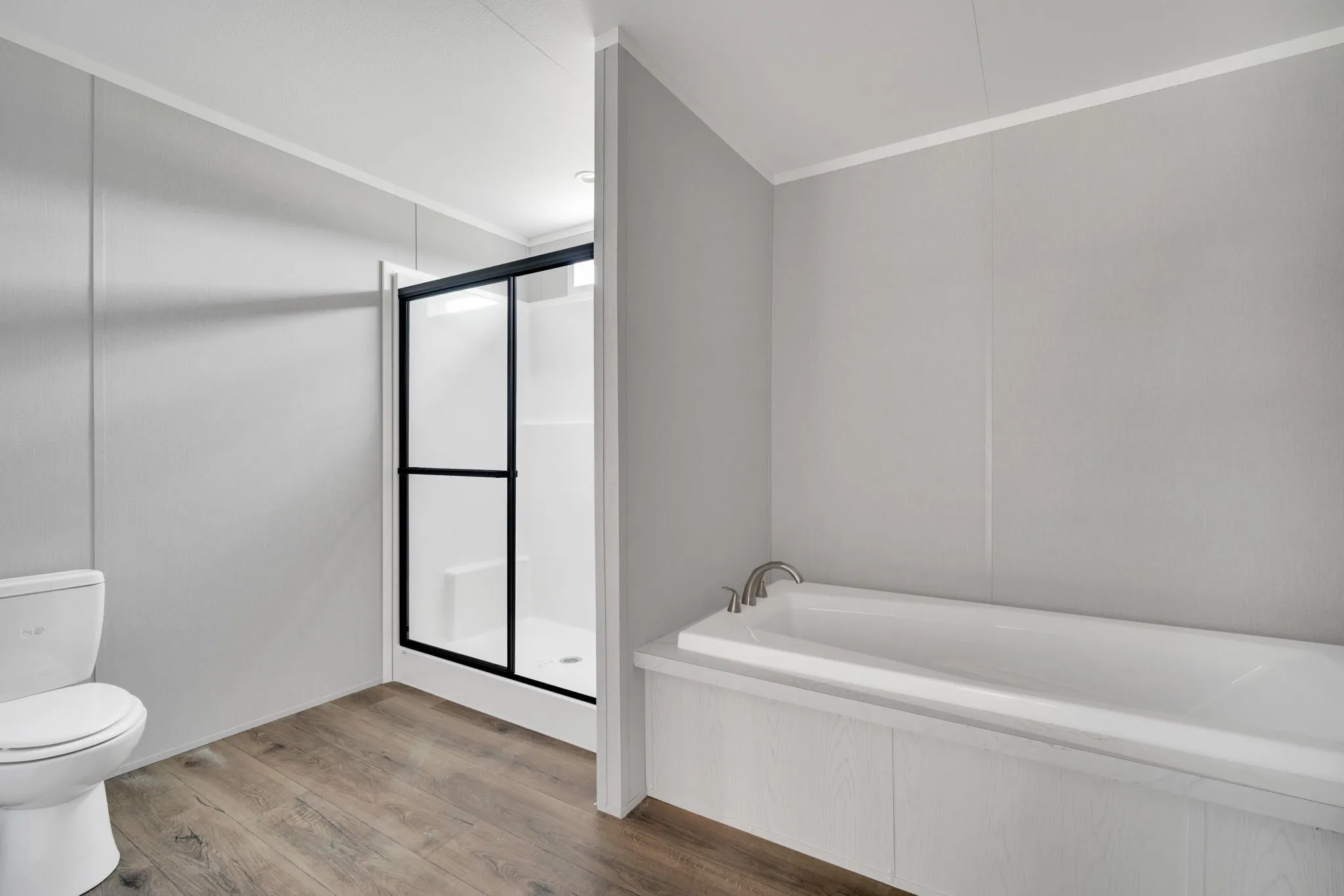 Bathroom featuring a built-in tub, a walk-in shower with black-framed sliding doors, a white toilet, and wood-finish flooring