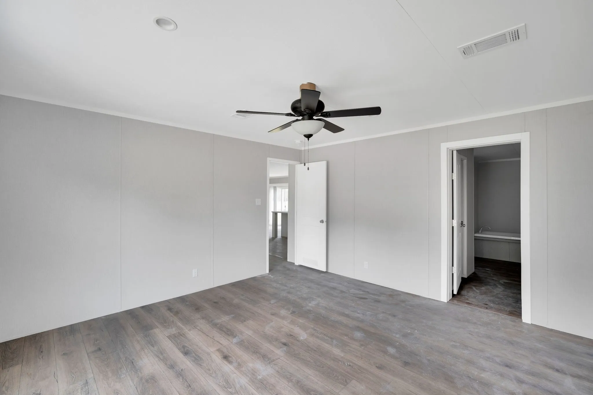 Spacious room featuring wood-finish flooring, light gray wall panels, and white trim