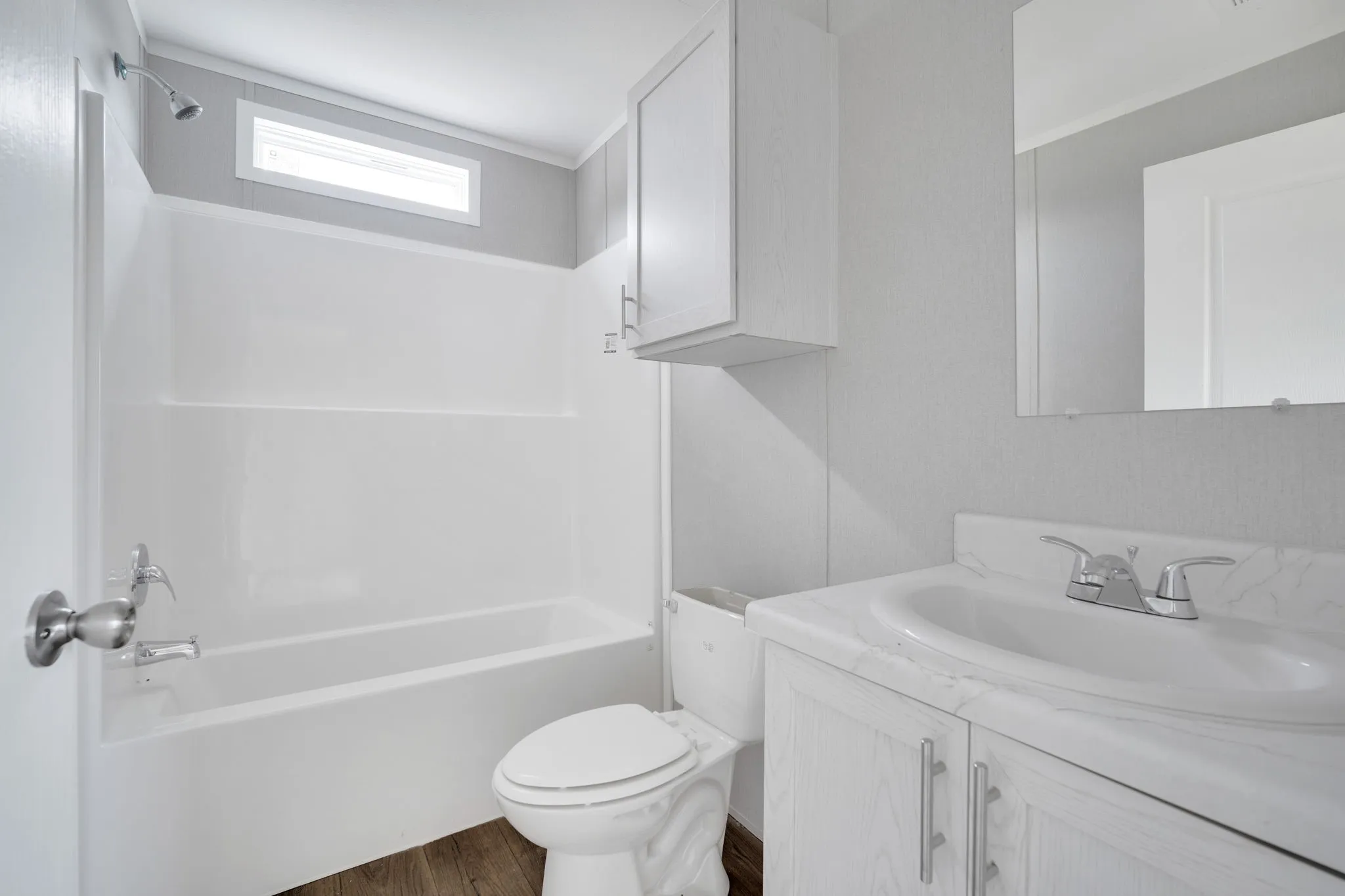 Bathroom featuring a white tub/shower combination with a horizontal window, wood-finish flooring, and a vanity with a white countertop and integrated sink