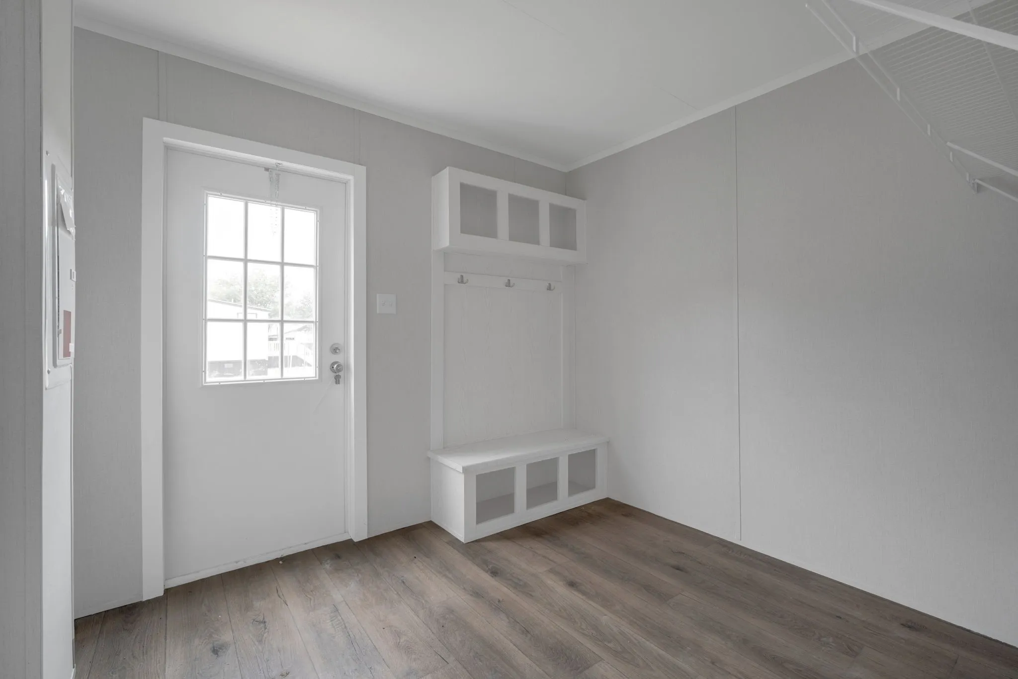Entryway featuring a six-pane windowed door, built-in storage bench with open compartments, upper cubby storage, coat hooks, and wood-finish flooring