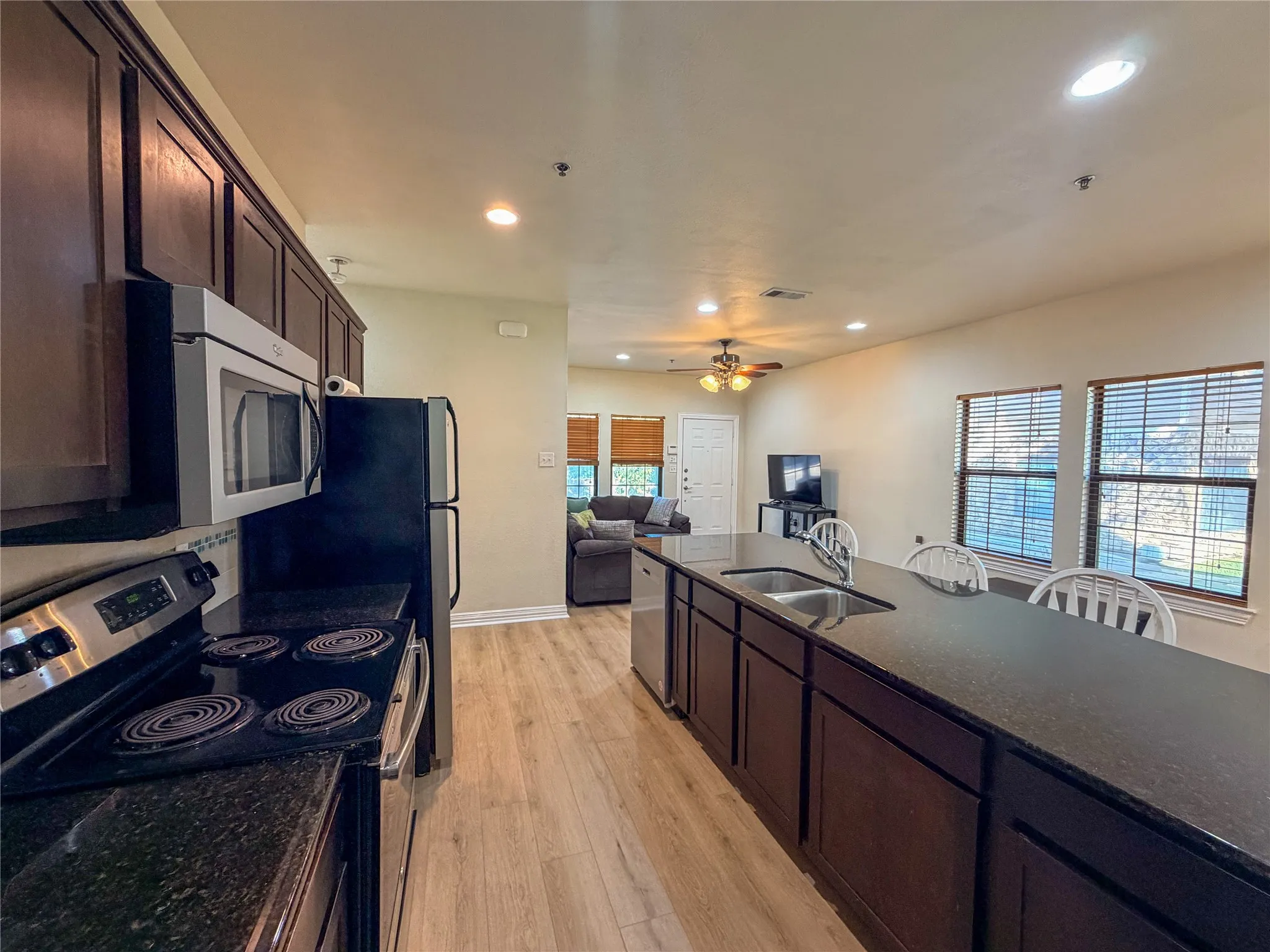Kitchen featuring dark wood cabinetry, stainless steel appliances, dark countertops, and wood-finish flooring