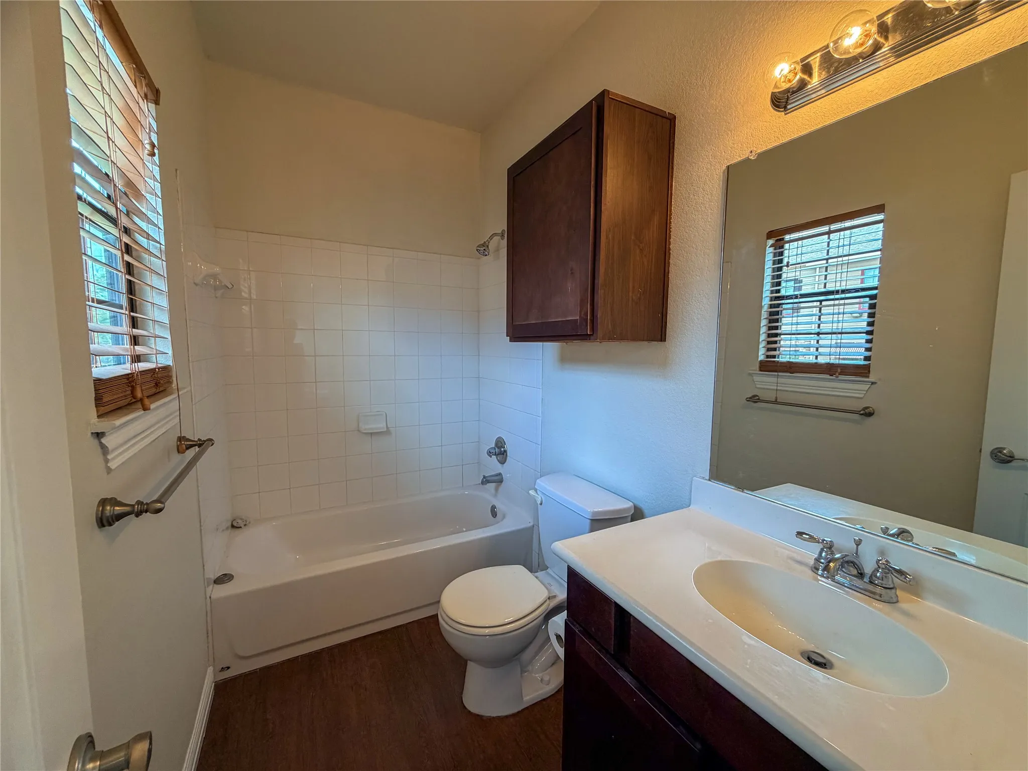 Bathroom 3:  featuring a white bathtub with tile surround, wood-finish flooring, a vanity with an integrated sink, and an overhead medicine cabinet