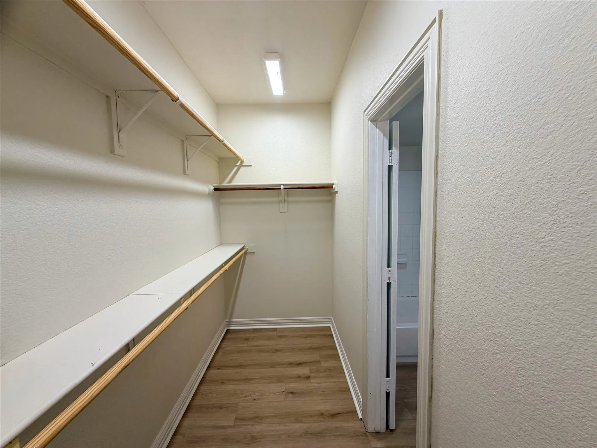 Walk-in closet with wood-finish flooring, built-in shelving, and hanging rods