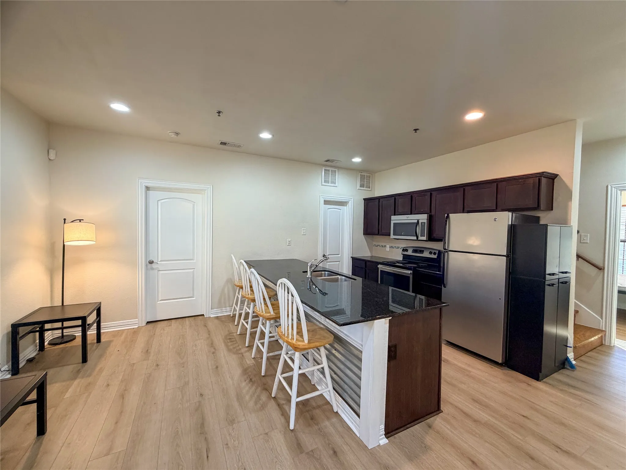 Open-concept living area with wood-finish flooring, recessed lighting, and a kitchen island featuring a dark countertop