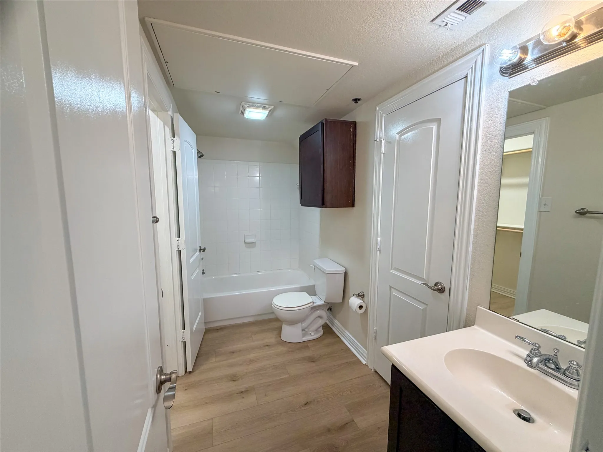 Bathroom 2 with White bathtub with subway tile surround, wood-finish flooring, dark wood-finish vanity with white countertop, and chrome fixtures