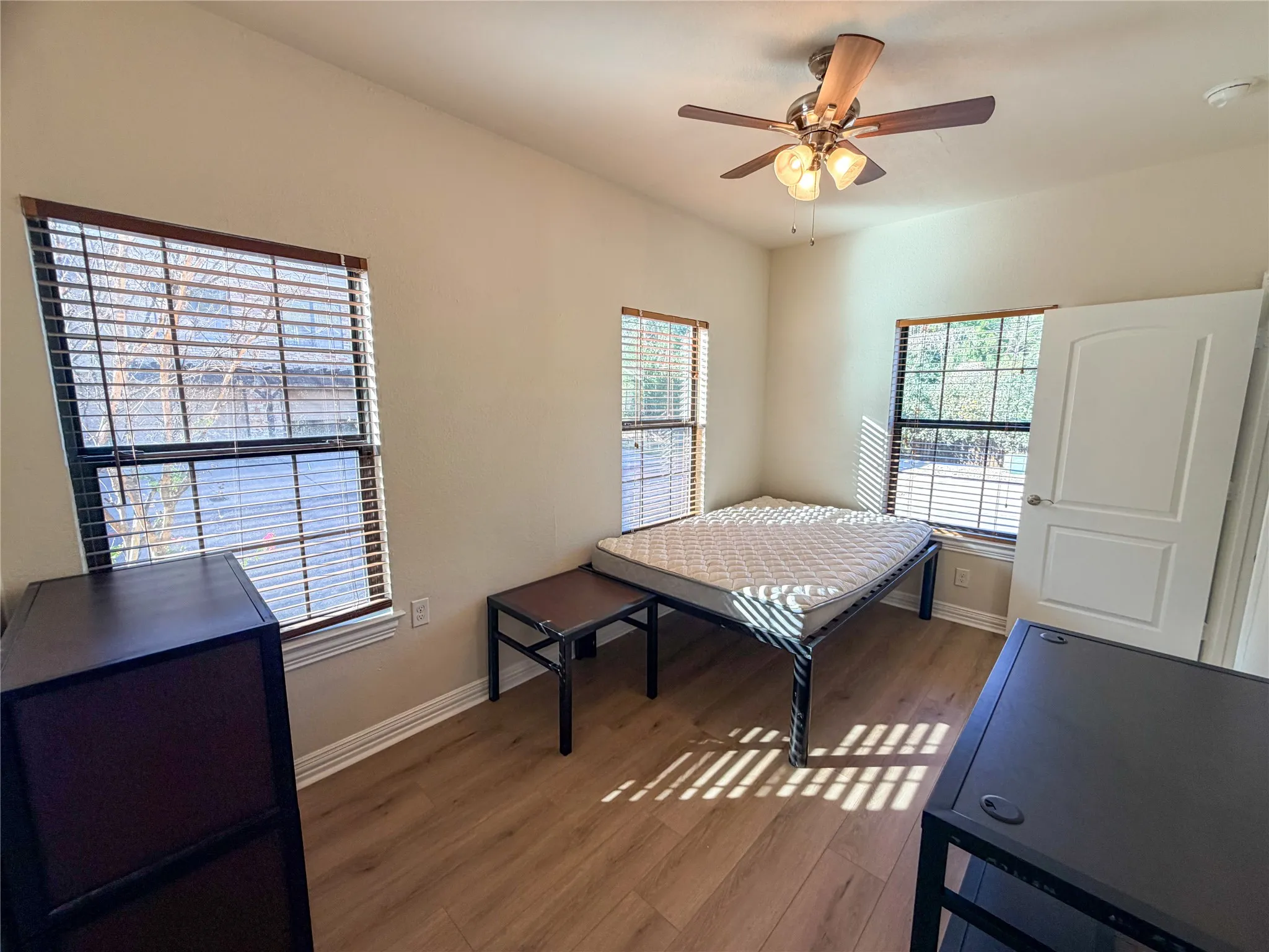 Bedroom 1 featuring dual windows with blinds, wood-finish flooring, and a ceiling fan with integrated lighting