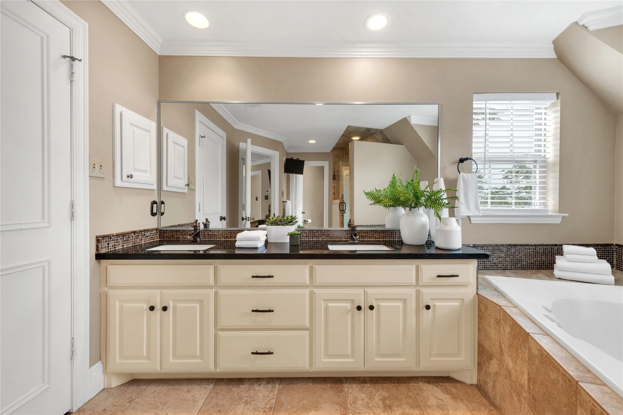 Bathroom vanity featuring dual under-mount sinks, a black countertop, and a large wall-mounted mirror