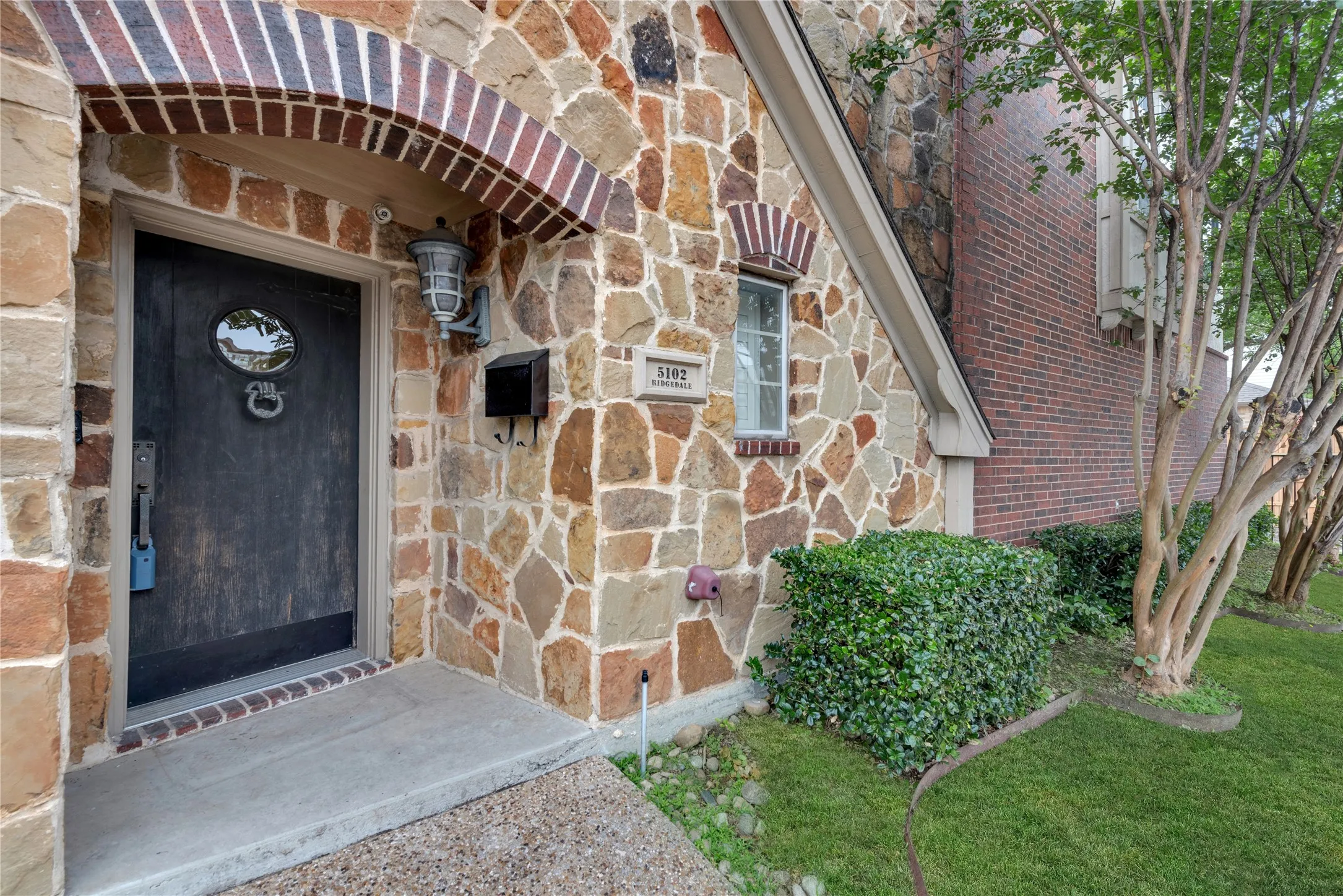 Stone façade entryway featuring a dark wood-finish door with an oval window and decorative knocker