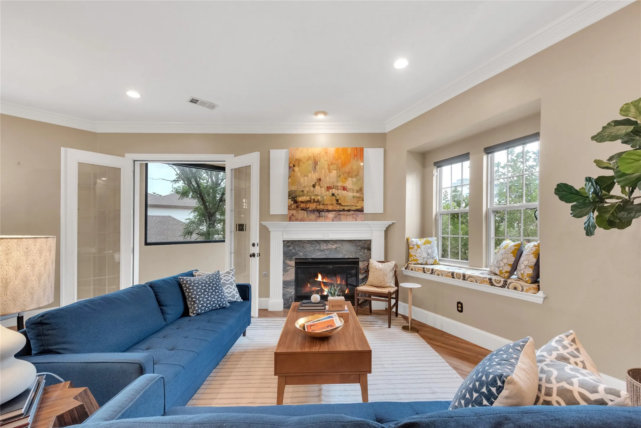 Living room featuring a fireplace with stone surround and white mantel, hardwood flooring, and a window seat with cushion