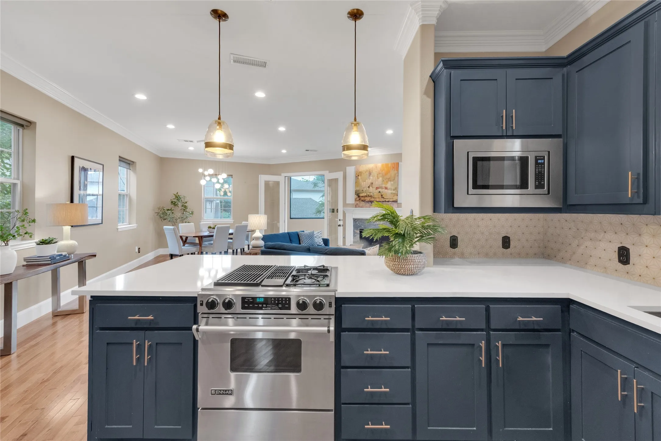 Kitchen featuring a stainless steel range with a gas cooktop, white countertops, dark blue cabinetry with brushed nickel hardware, a built-in microwave, and a textured tile backsplash