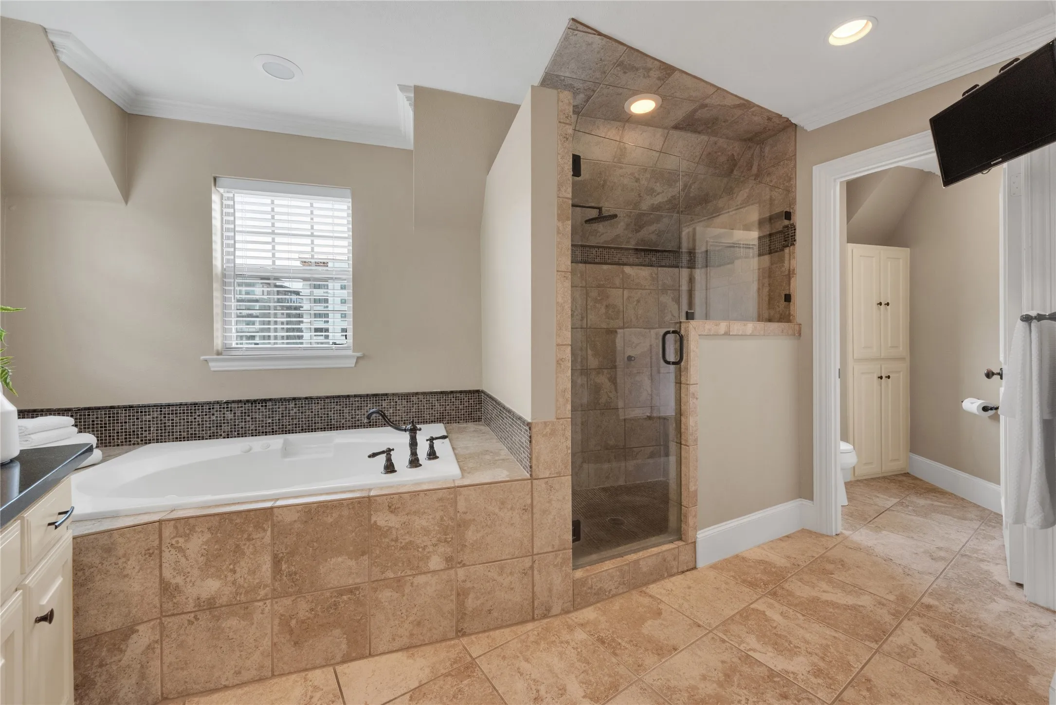 Spacious bathroom featuring a built-in tub with dark bronze fixtures, a tiled surround, and a mosaic tile backsplash