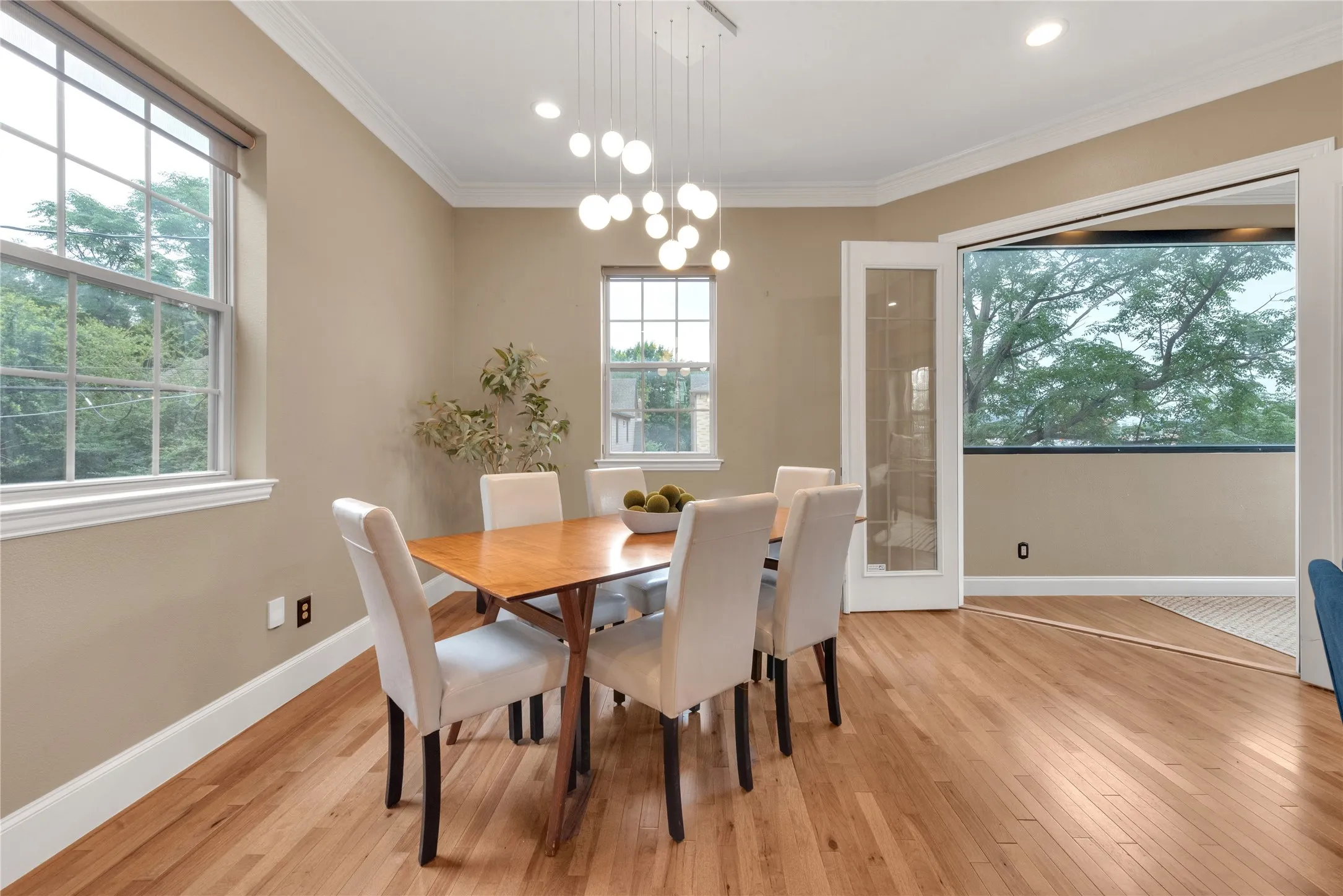 Dining area featuring hardwood flooring, crown molding, a contemporary chandelier, multiple windows, and glass-paneled French doors
