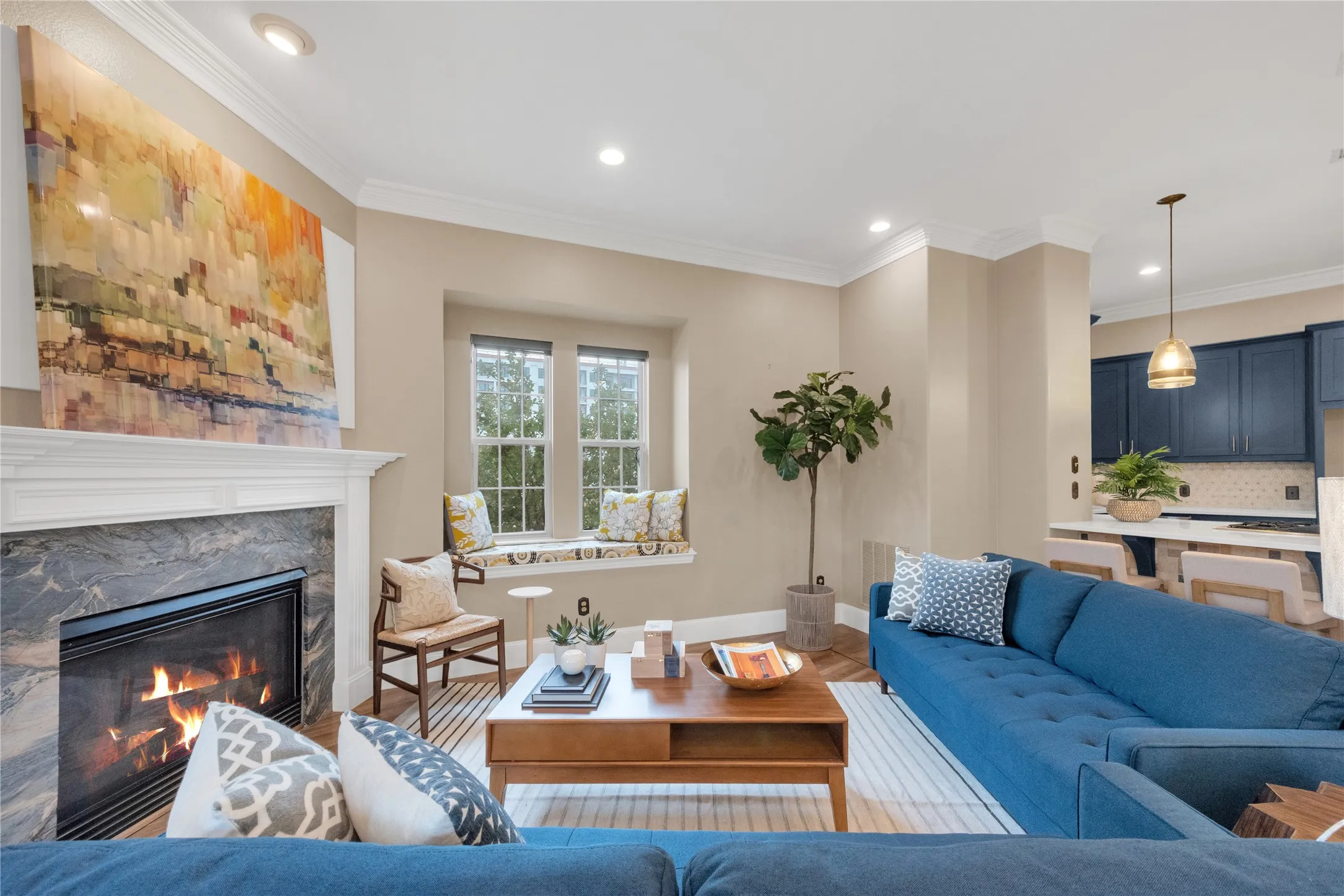 Living area featuring a fireplace with a stone surround and a substantial mantel, recessed lighting, crown molding, a built-in window seat, and wood-finish flooring