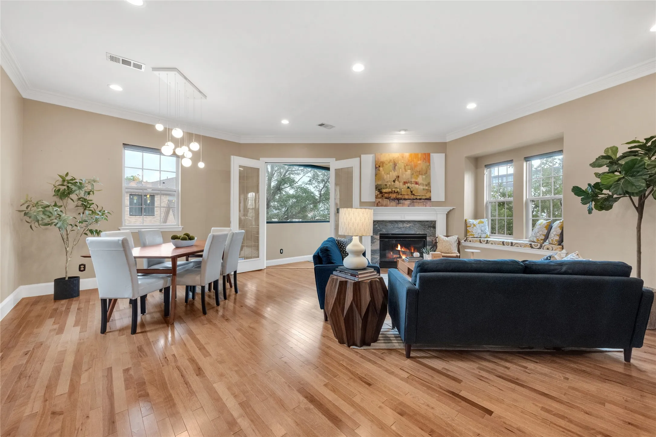 Spacious living area featuring warm wood-finish flooring, a contemporary fireplace with a stone surround and white mantle, and recessed lighting