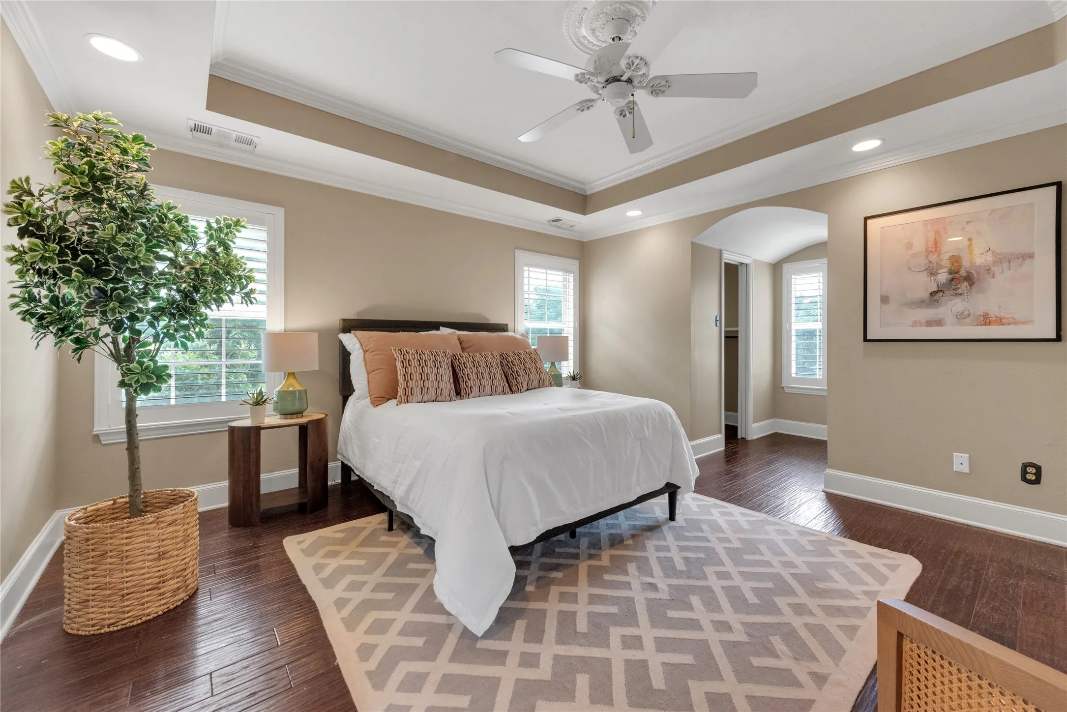 Hardwood flooring throughout this room featuring a tray ceiling with a ceiling fan