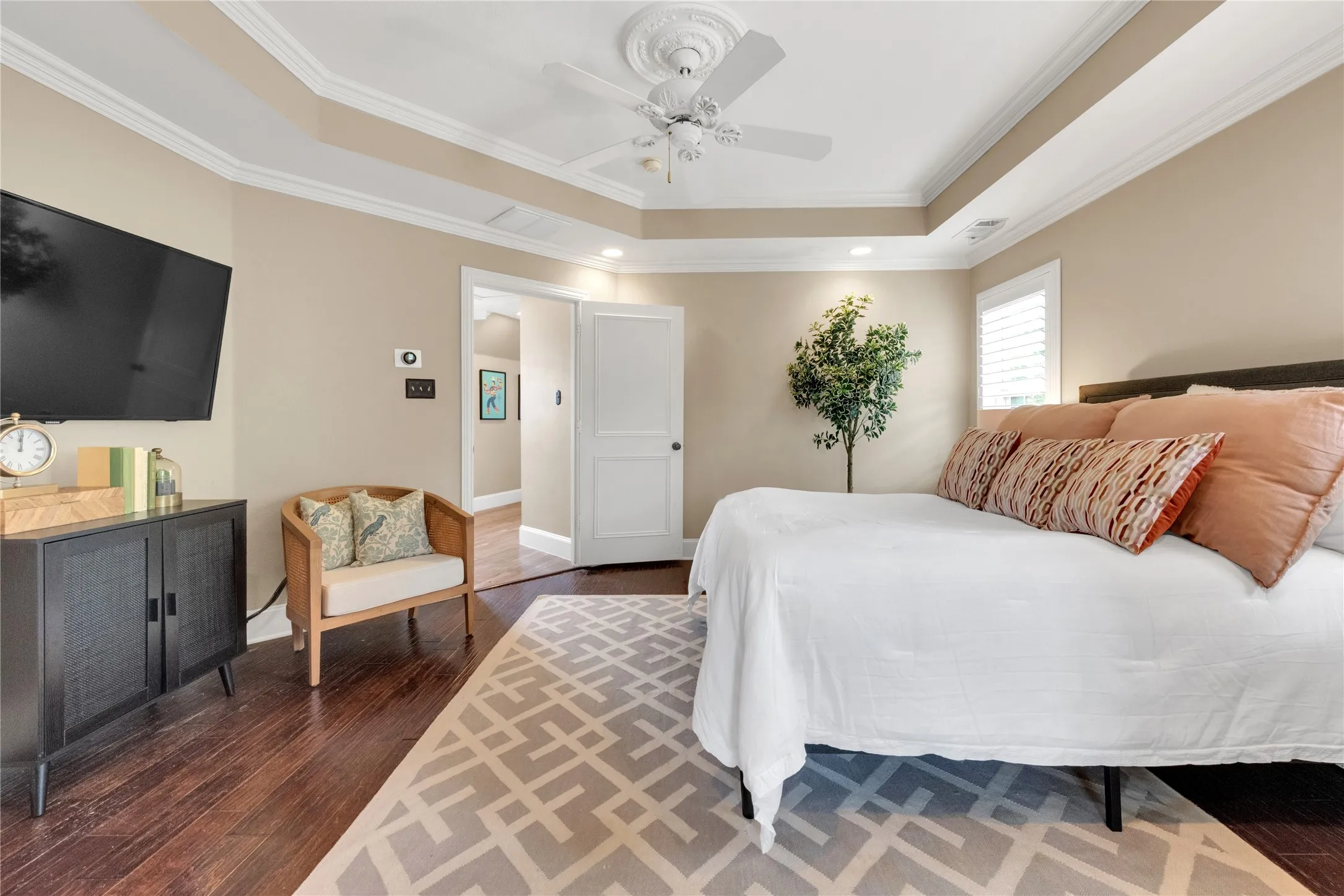 Tray ceiling with crown molding, ceiling fan, dark wood-finish flooring, plantation shutters, and recessed lighting