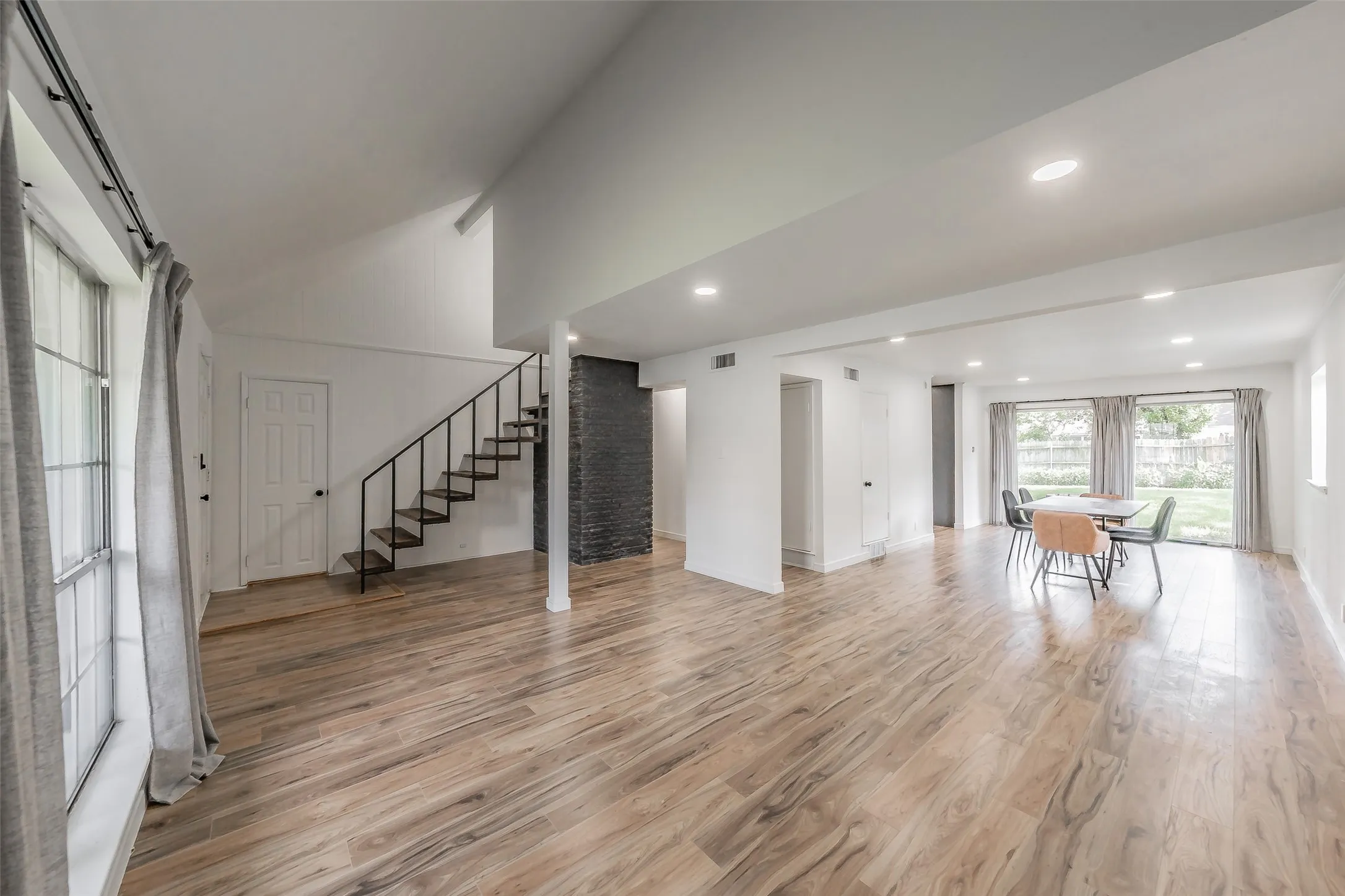 Open-concept living space featuring wood-finish flooring, recessed lighting, and a prominent staircase with metal railing