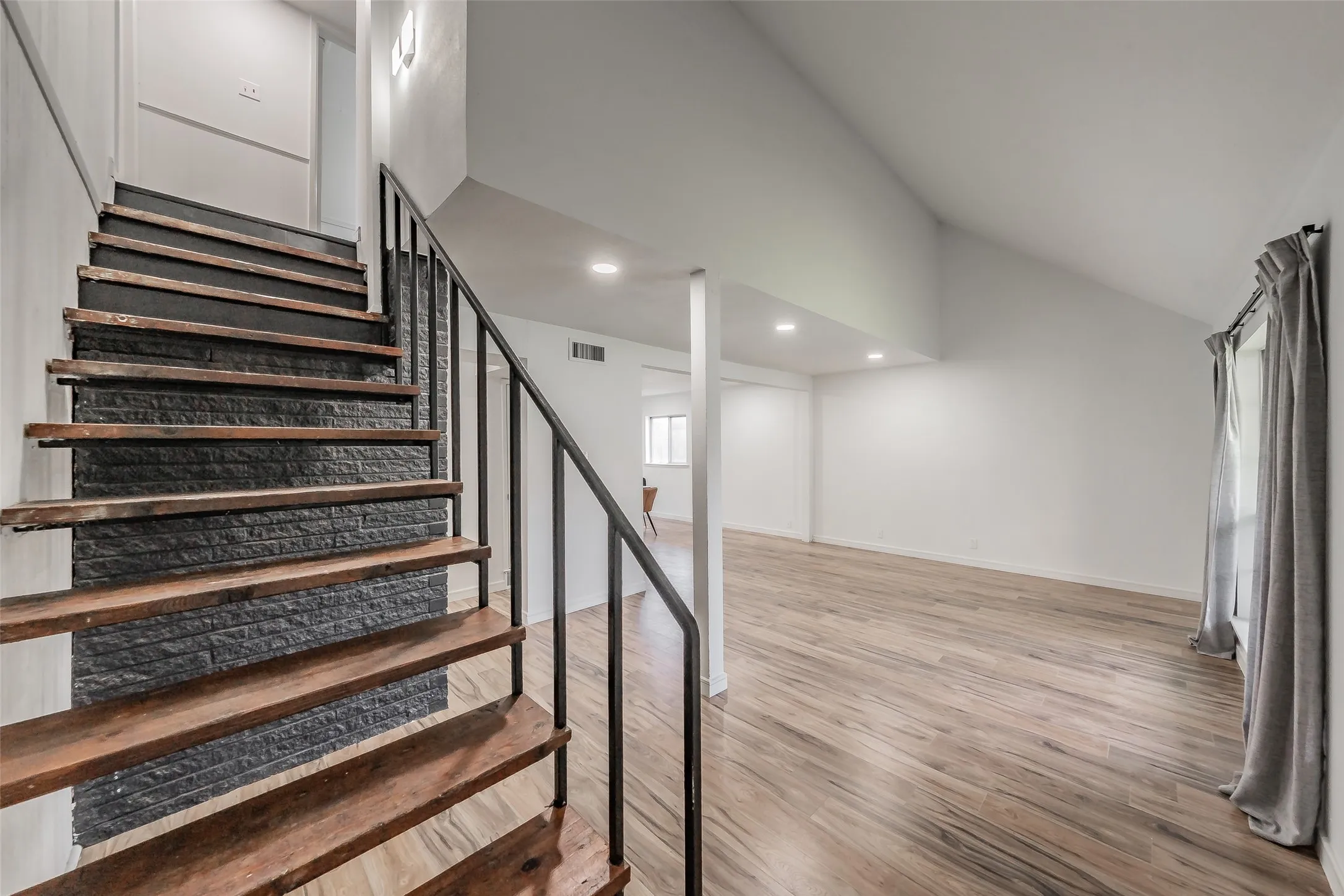 Hardwood staircase with a textured dark stone accent wall and black metal railing