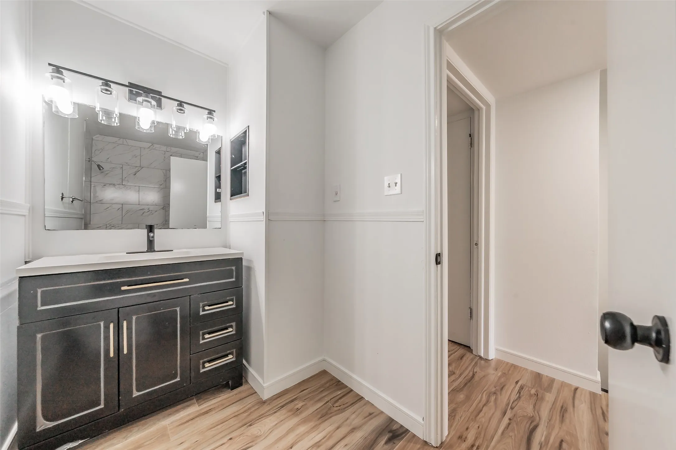 Bathroom vanity featuring a dark wood cabinet with silver-toned hardware, a light-colored countertop, and a rectangular mirror