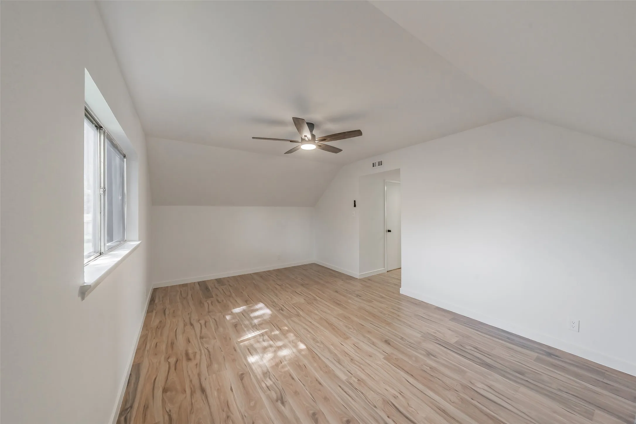 Bright room featuring wood-finish flooring, a contemporary ceiling fan, and a wide window