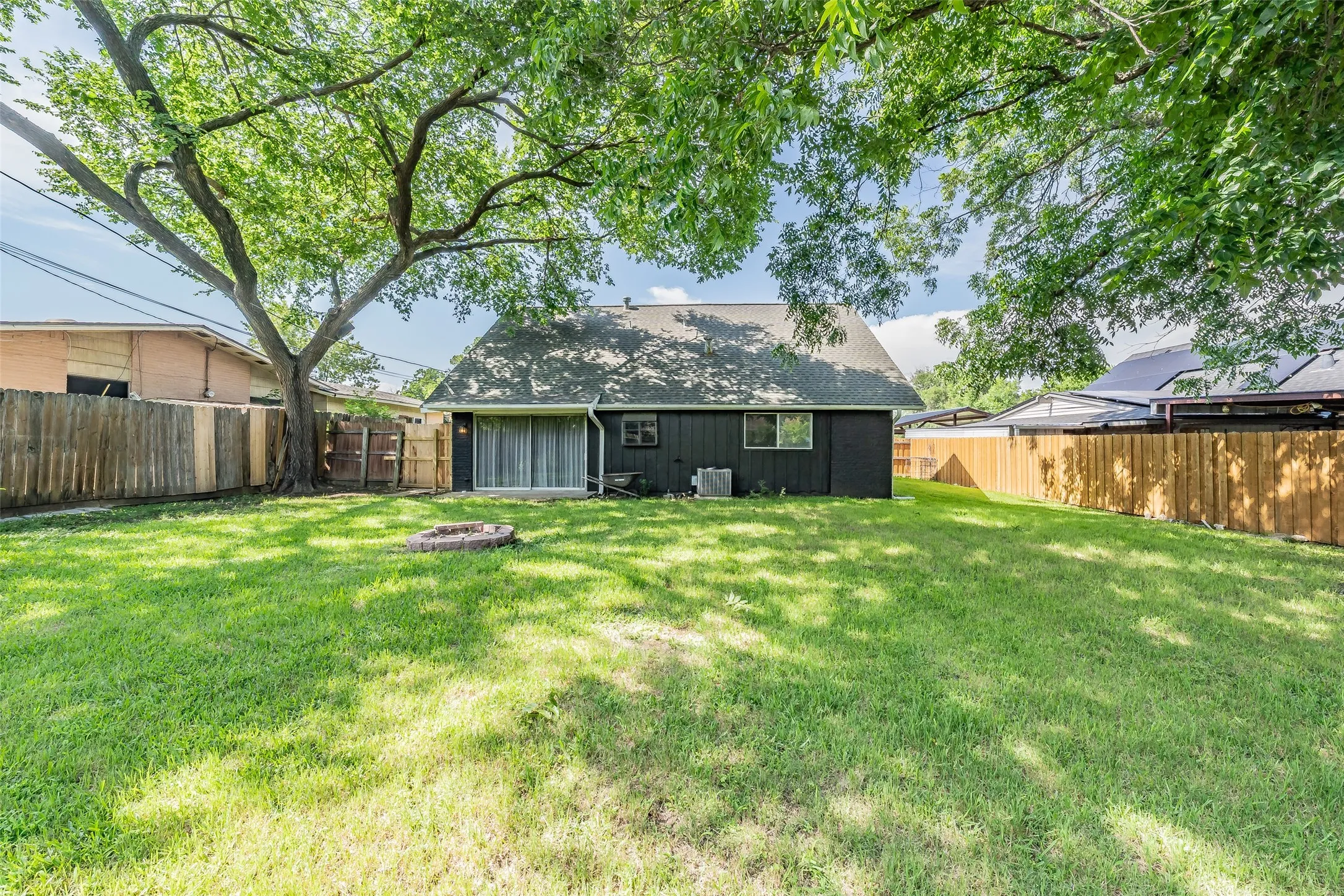 Expansive grassy yard featuring a dark exterior home with a partial privacy fence