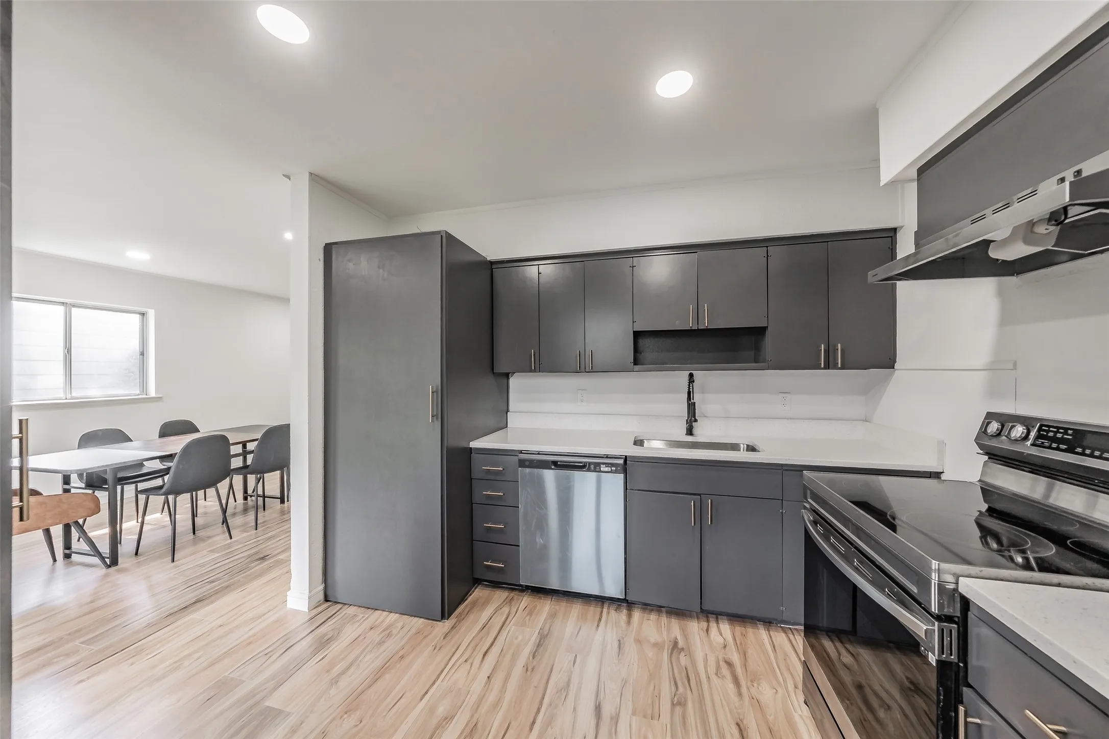 Modern kitchen featuring dark cabinetry, white countertops, stainless steel appliances, and wood-finish flooring