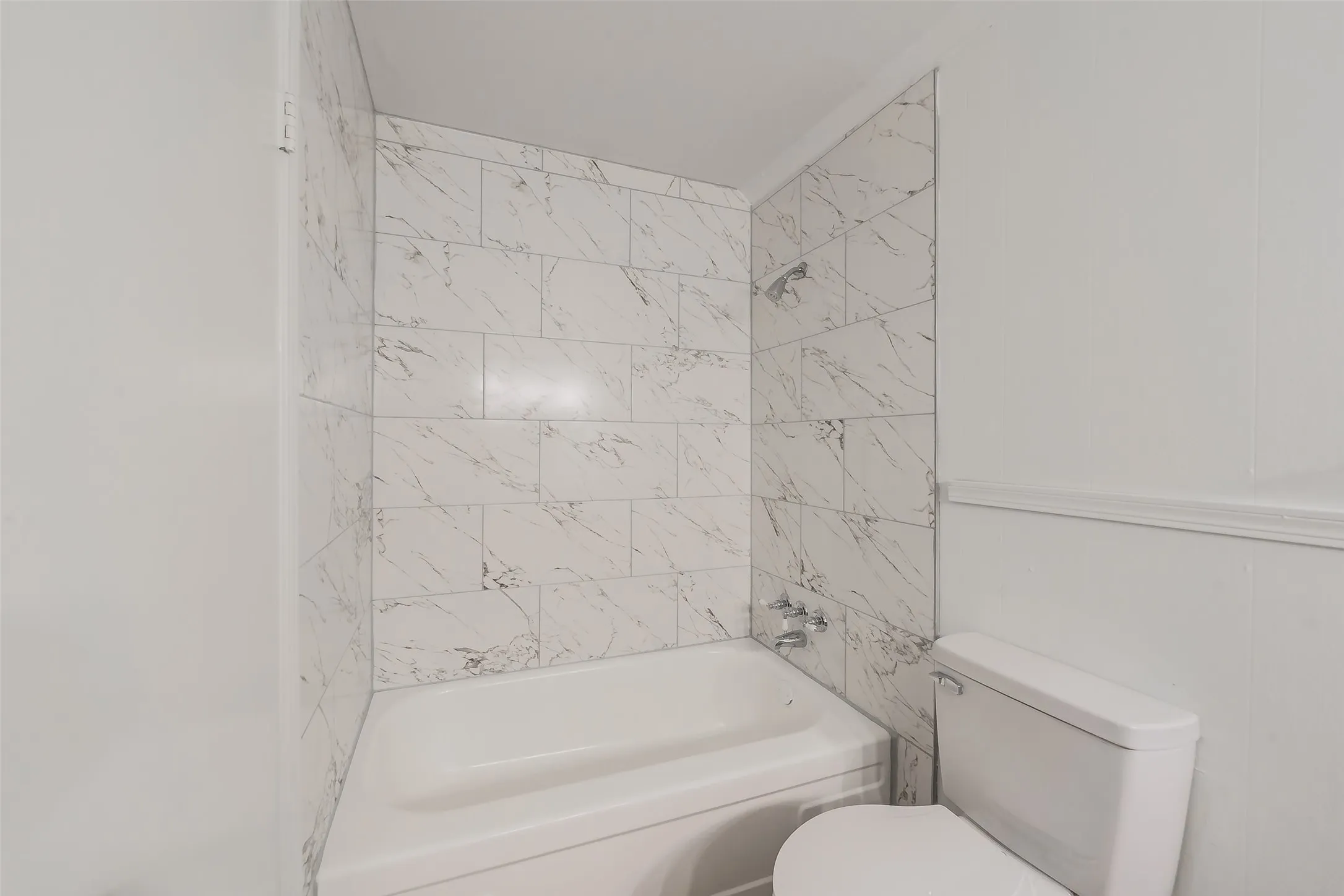 Bathroom featuring a white bathtub, white and gray veined subway tile surround, chrome shower fixtures, and a white toilet