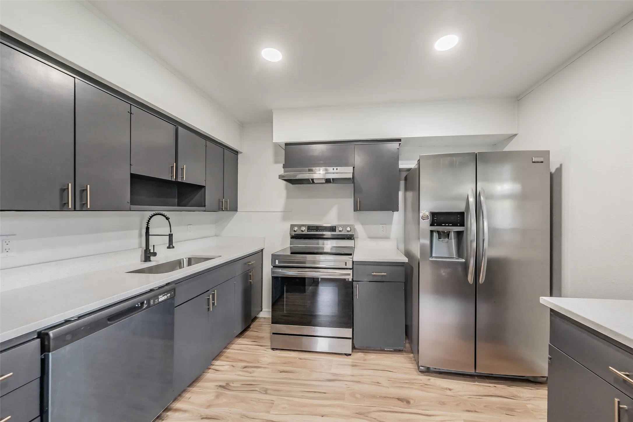 Kitchen featuring dark cabinetry with brushed nickel hardware, stainless steel appliances, light countertops, and wood-finish flooring
