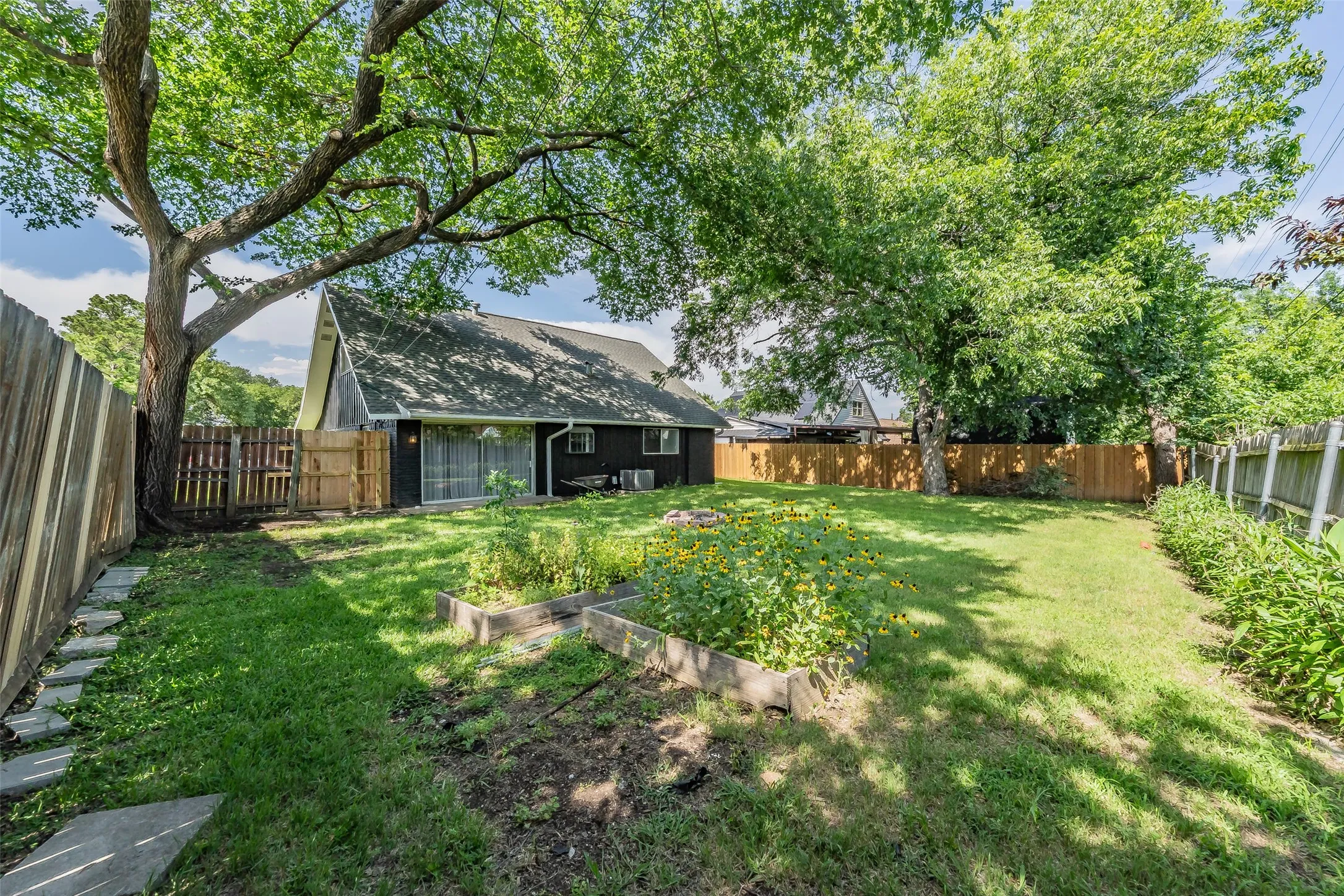 Spacious backyard featuring a lush lawn, mature trees, and raised garden beds