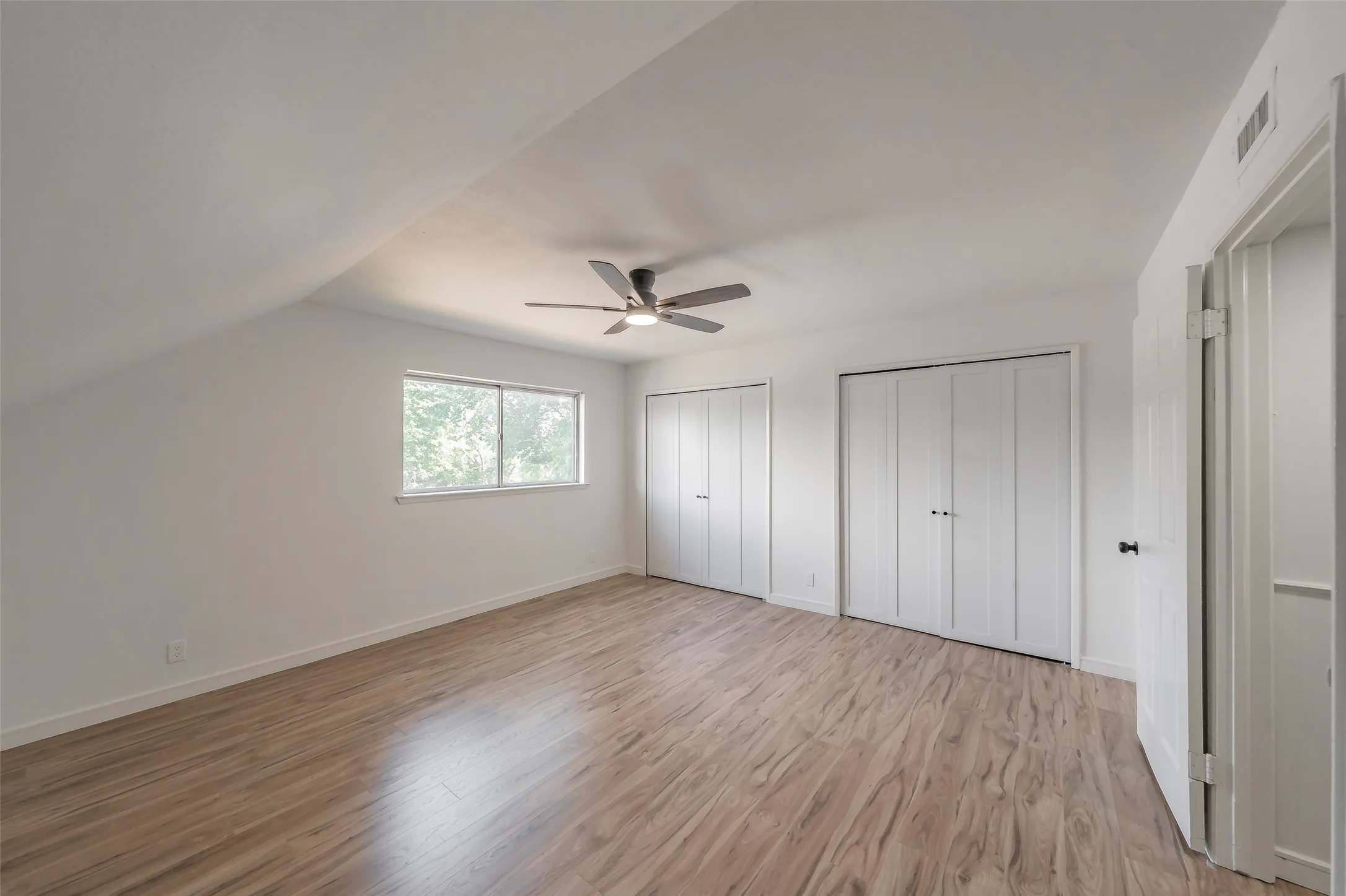 Room featuring wood-finish flooring, two sets of bi-fold closet doors, a single window, and a ceiling fan with integrated lighting