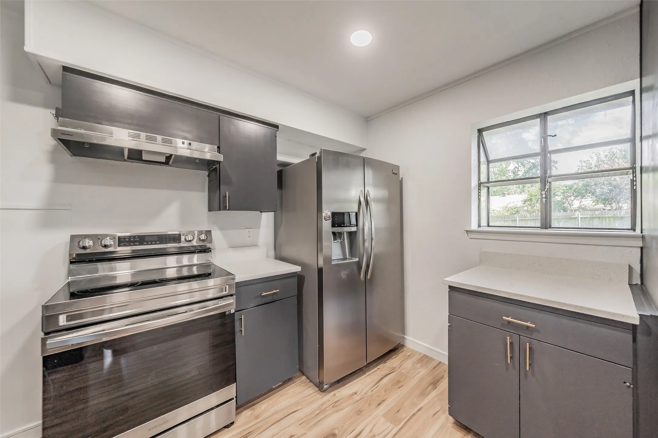 Kitchen featuring dark cabinetry, light countertops, wood-finish flooring, stainless steel appliances, and a window