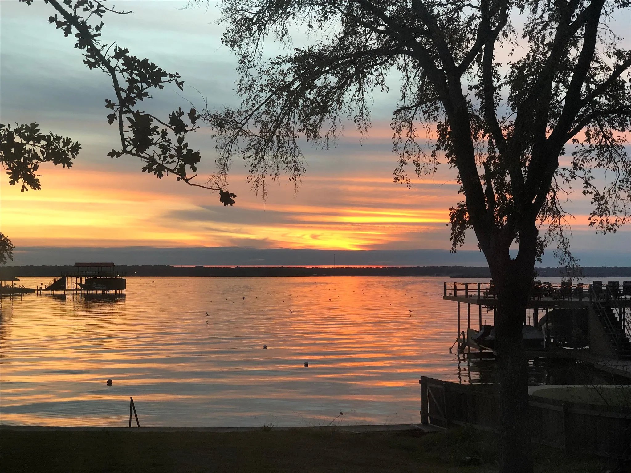 Expansive water frontage featuring a private dock with a boat lift, an additional covered boat house, and a separate fenced waterside area