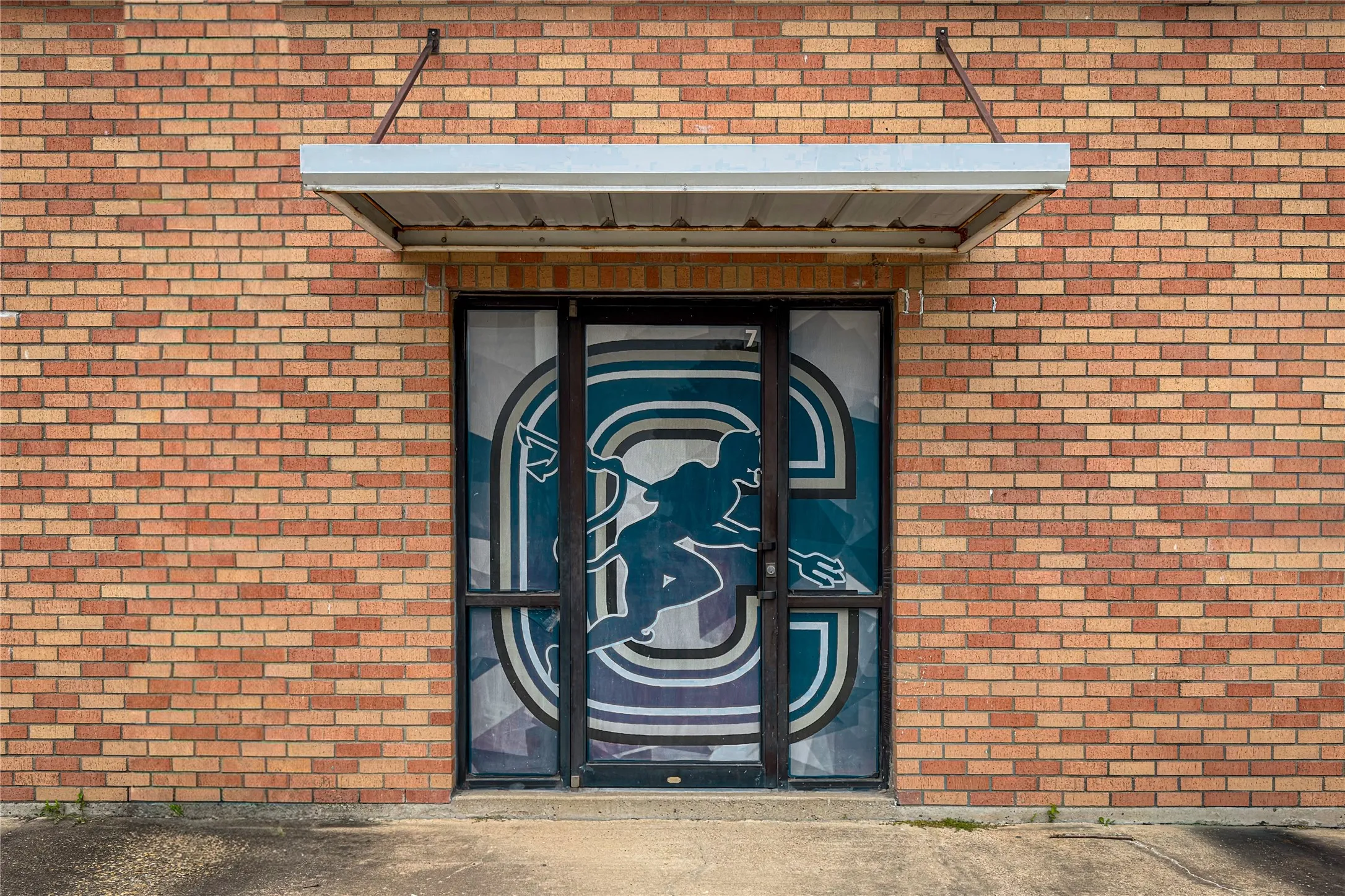 Brick exterior featuring a glass entrance with decorative film, an aluminum awning, and concrete ground-level approach
