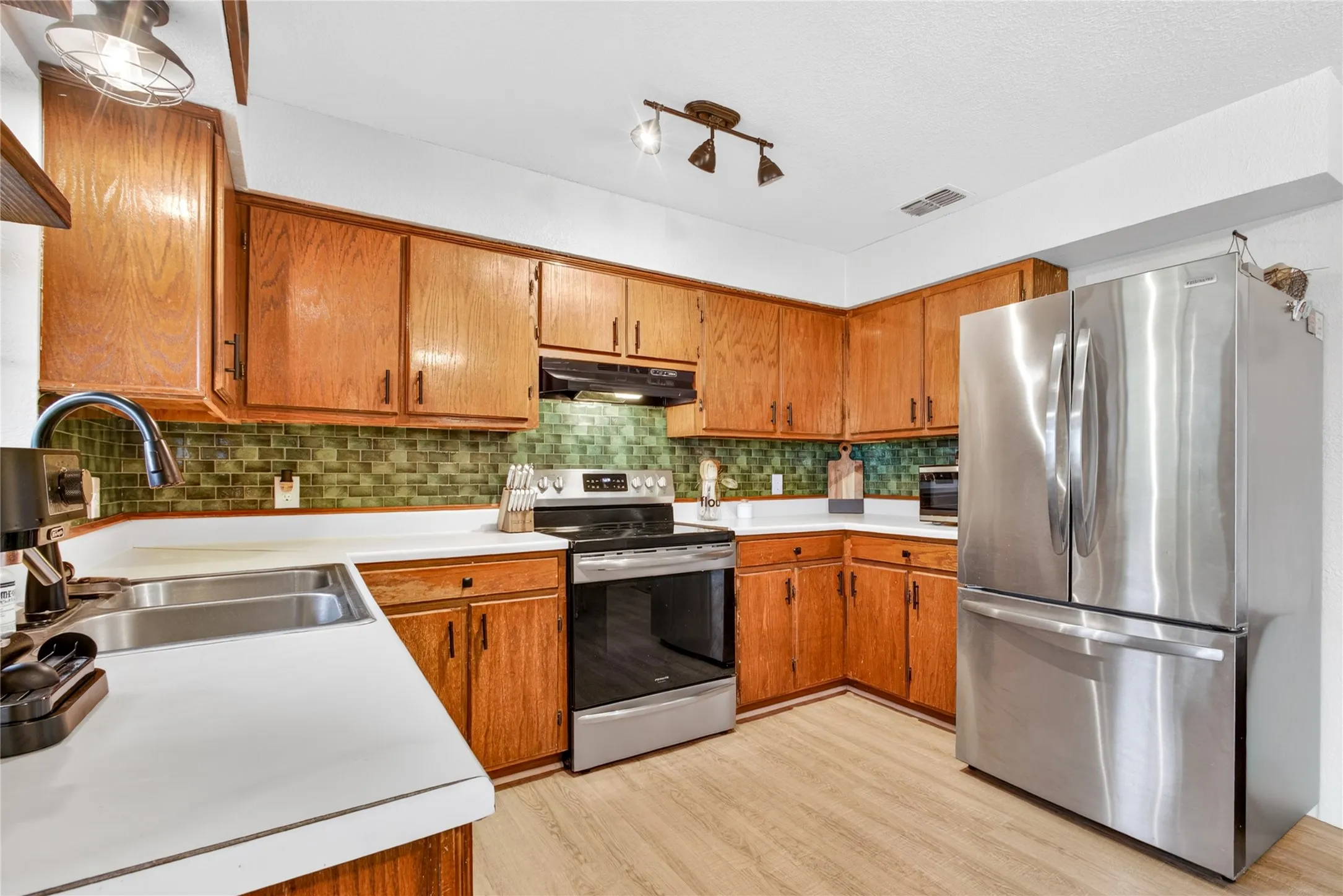 Kitchen featuring wood cabinetry, stainless steel appliances, a green tile backsplash, and white countertops