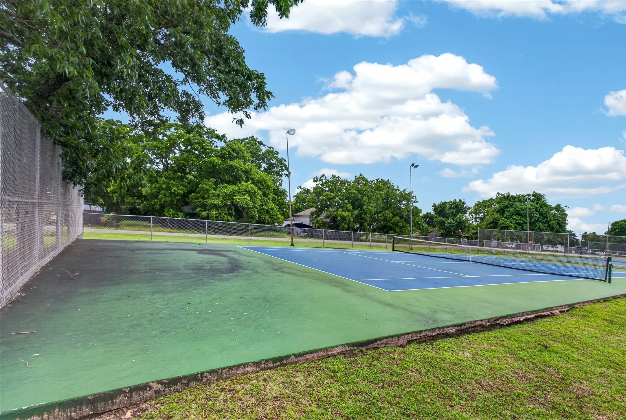 Outdoor tennis court with a blue playing surface and green surrounds