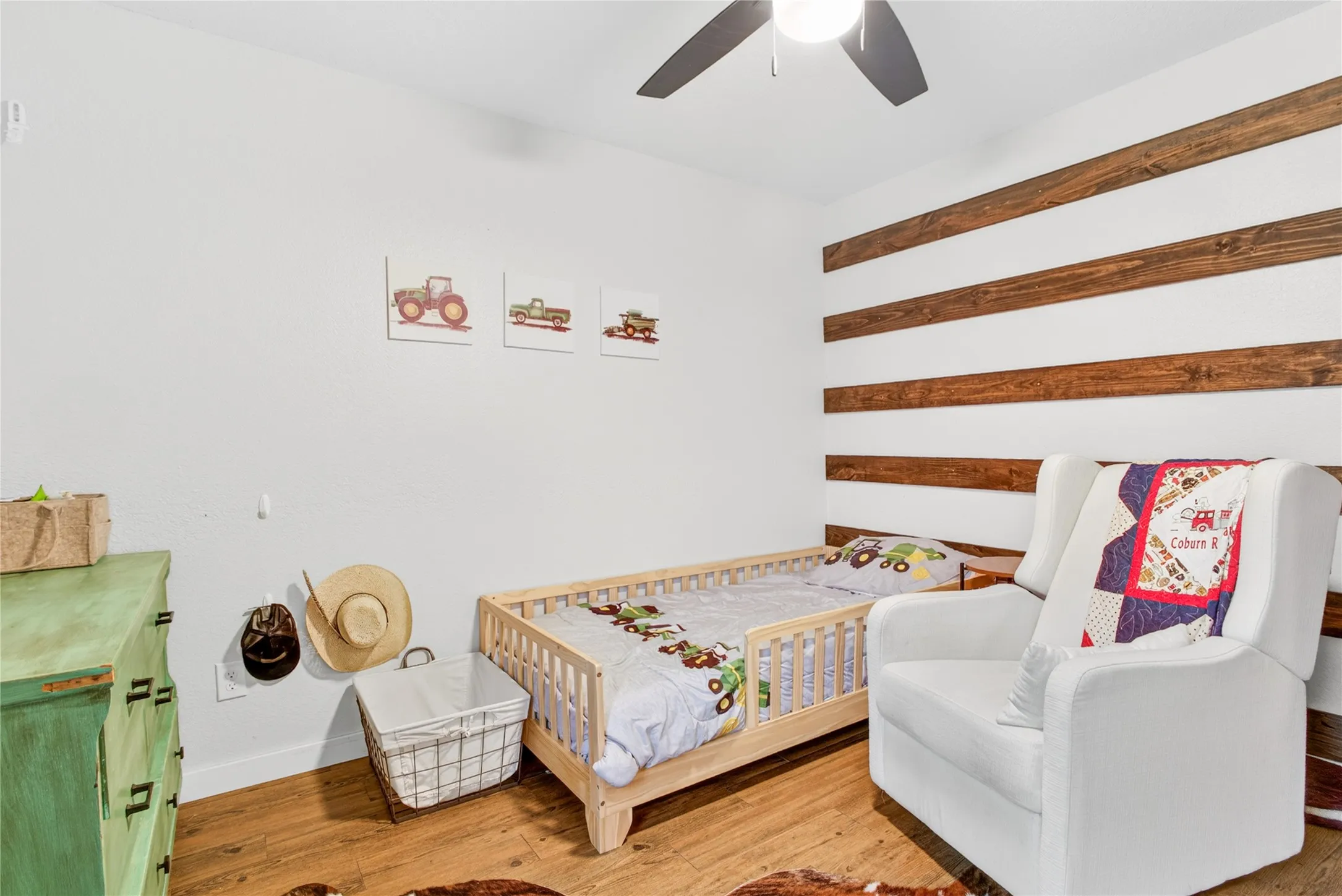 Room featuring wood-finish flooring, a ceiling fan, and a distinctive accent wall with horizontal wood paneling