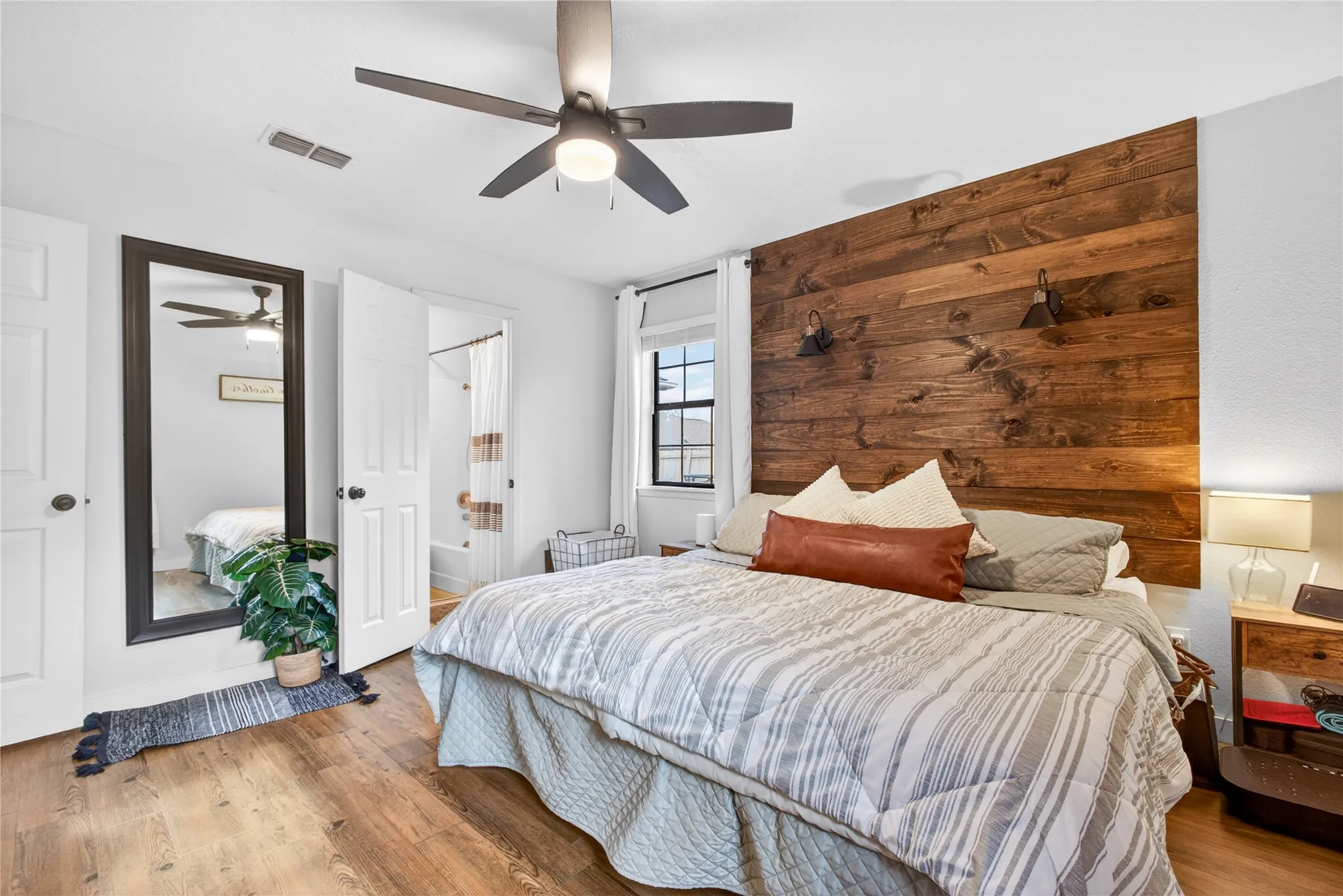 Bedroom featuring a decorative wood-panel accent wall, wood-finish flooring, a ceiling fan with integrated lighting, and a white paneled door