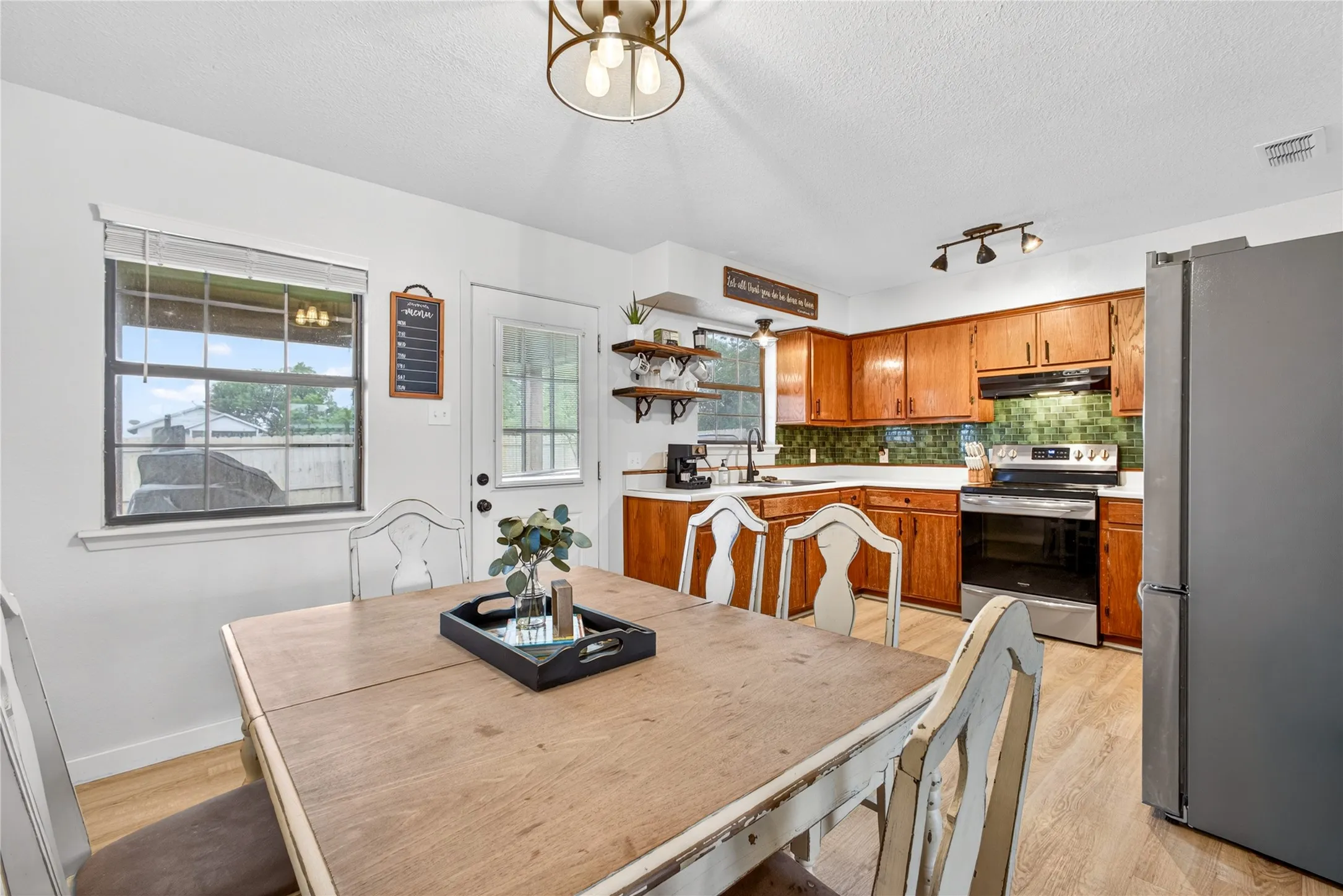 Kitchen dining space featuring wood-finish flooring, wood cabinetry, a tile backsplash, and stainless steel appliances