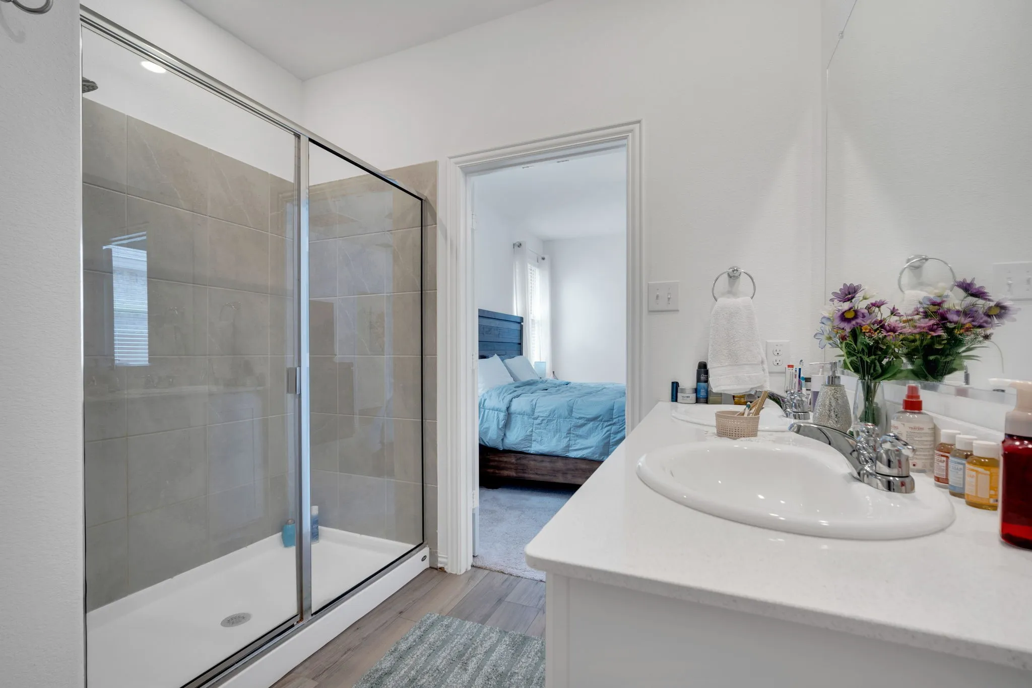 Bathroom featuring a glass-enclosed shower with tile surround, a dual vanity with undermount sinks and chrome fixtures, and wood-finish flooring