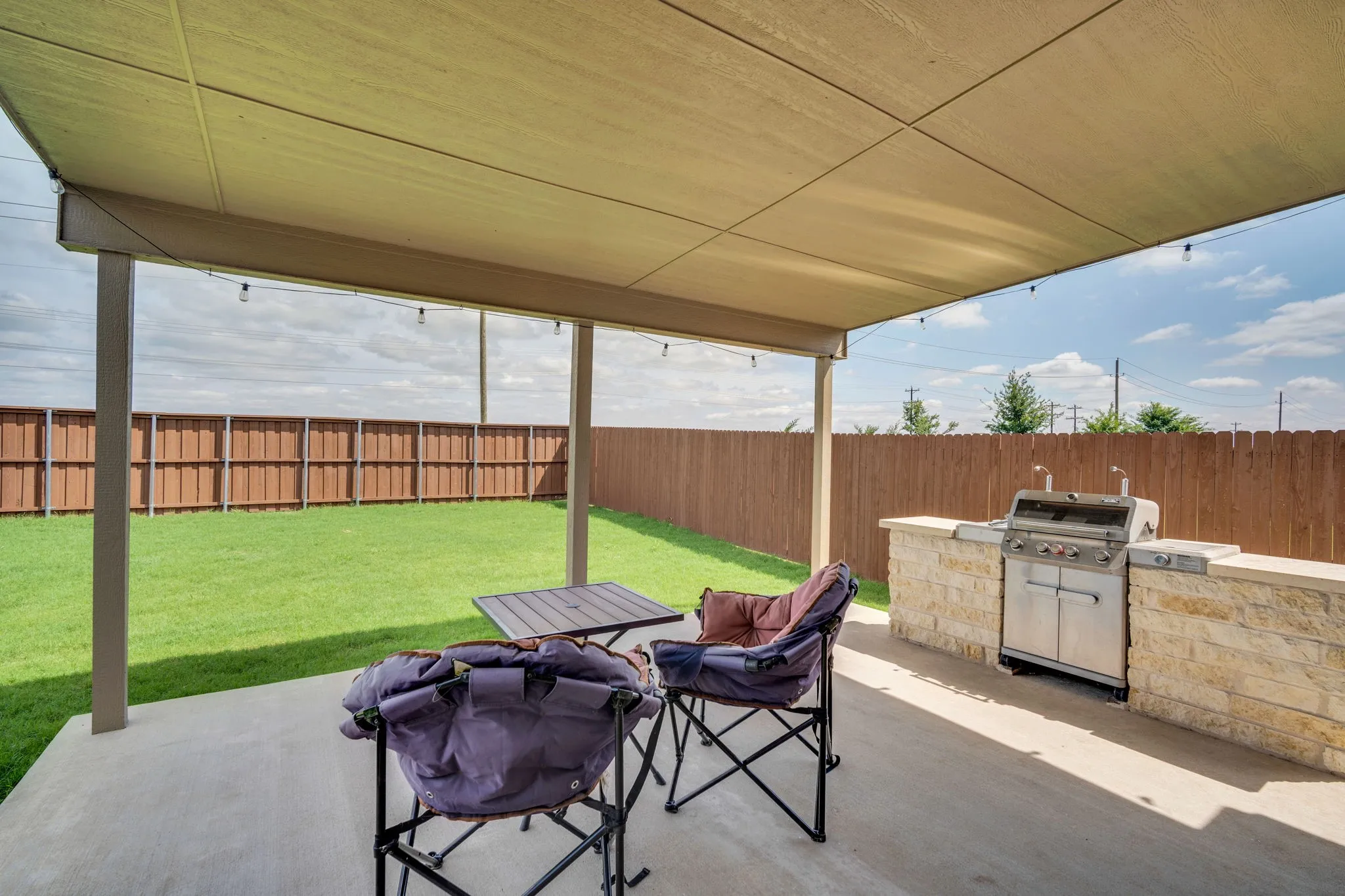 Covered concrete patio featuring an outdoor kitchen with stone-finish base, stainless steel grill, and concrete countertops