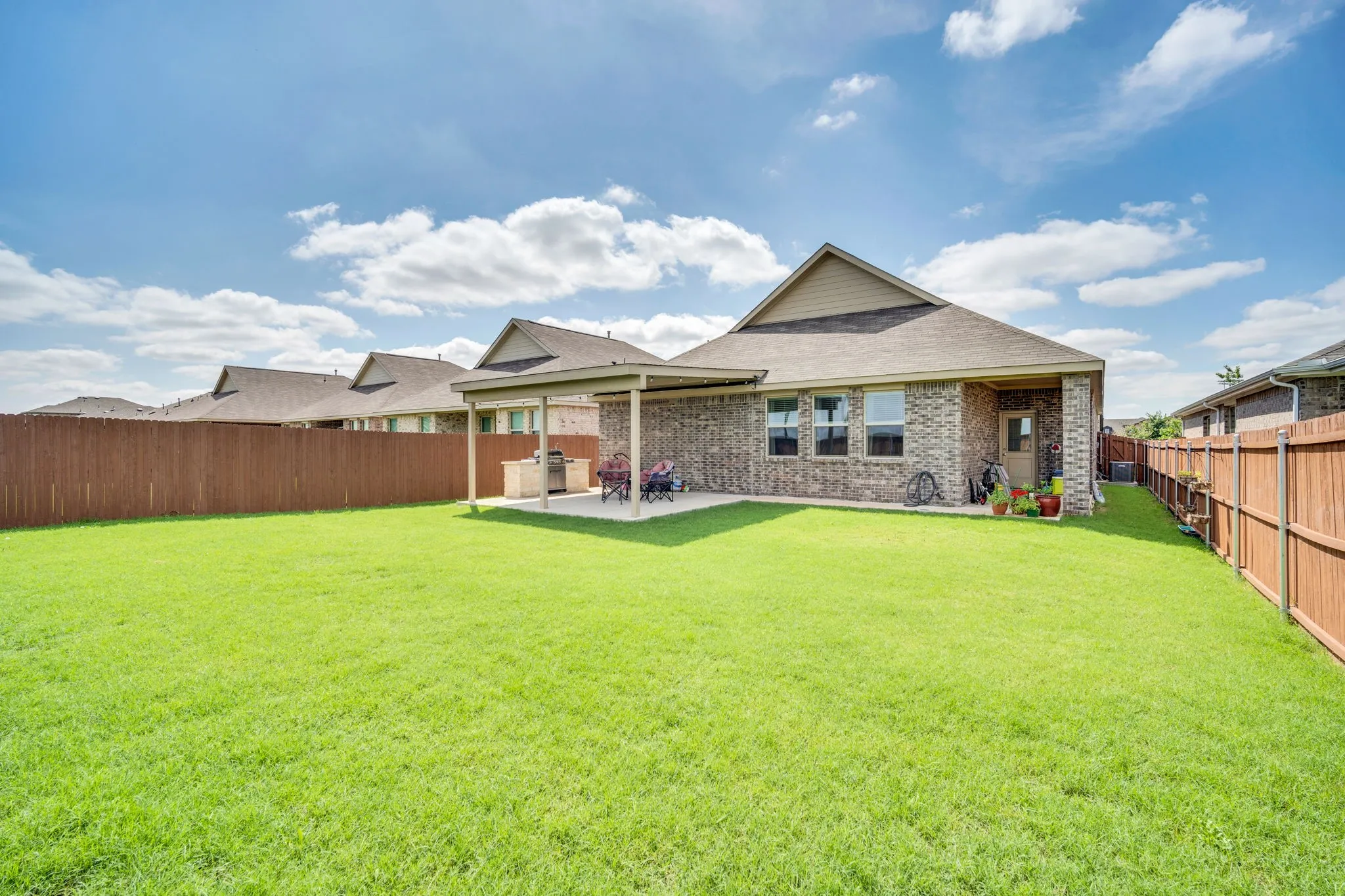 Expansive green lawn with a covered patio, featuring a built-in outdoor kitchen with stone-finish cabinetry and a grill, and privacy fencing