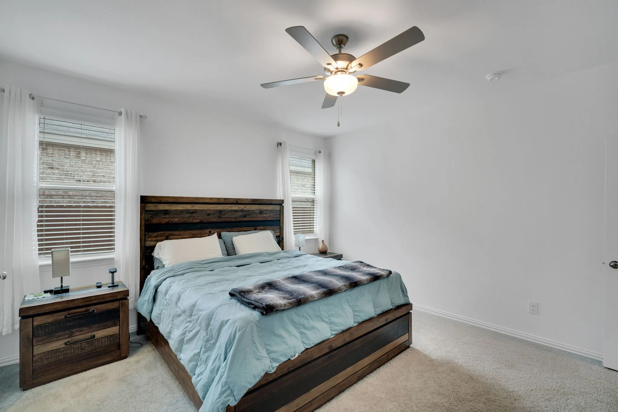 Carpeted bedroom featuring a ceiling fan with integrated lighting, white walls, and two windows with blinds