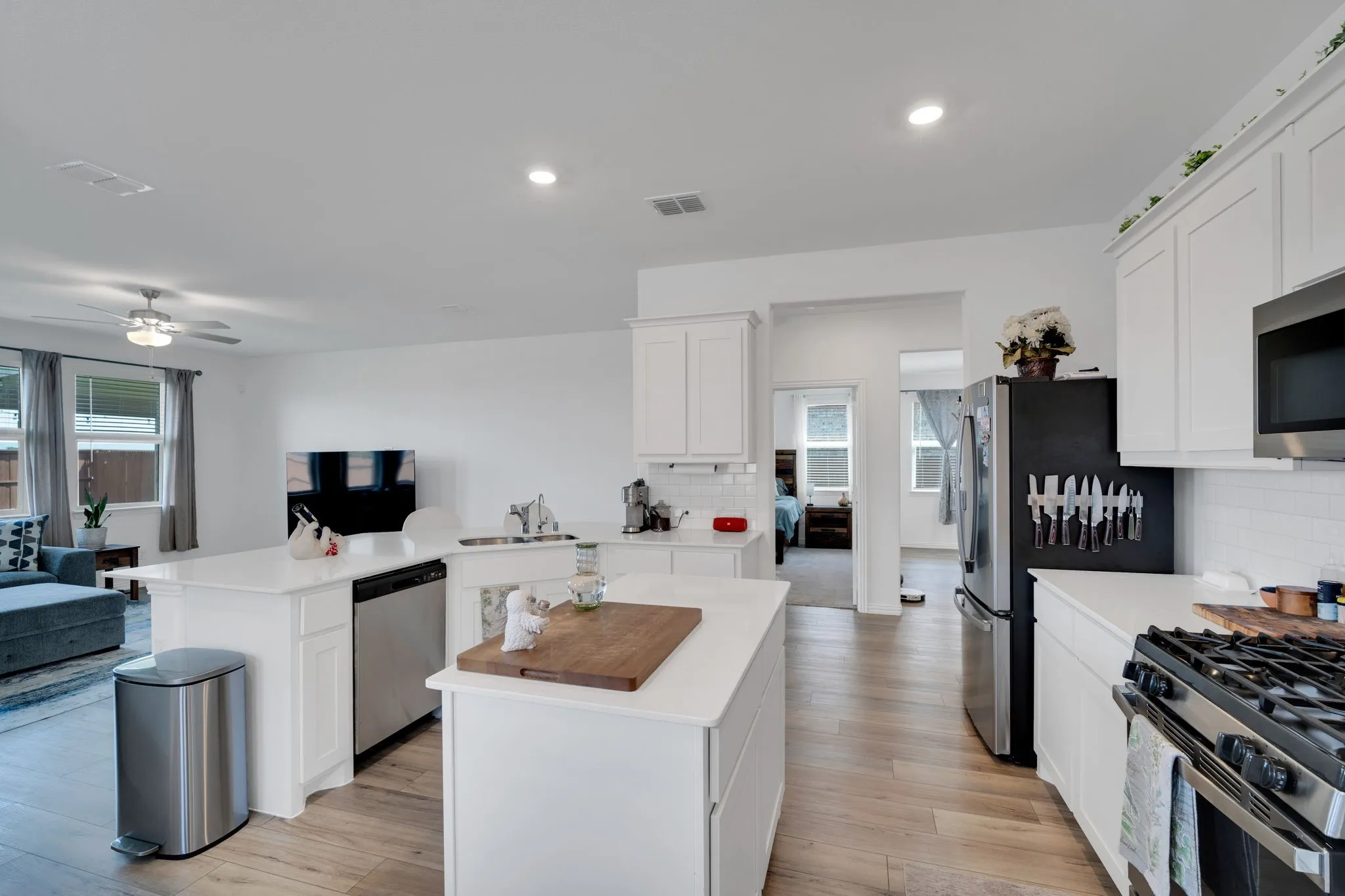 Open-concept kitchen featuring white cabinetry, light-toned countertops, and stainless steel appliances including a refrigerator, dishwasher, and gas range