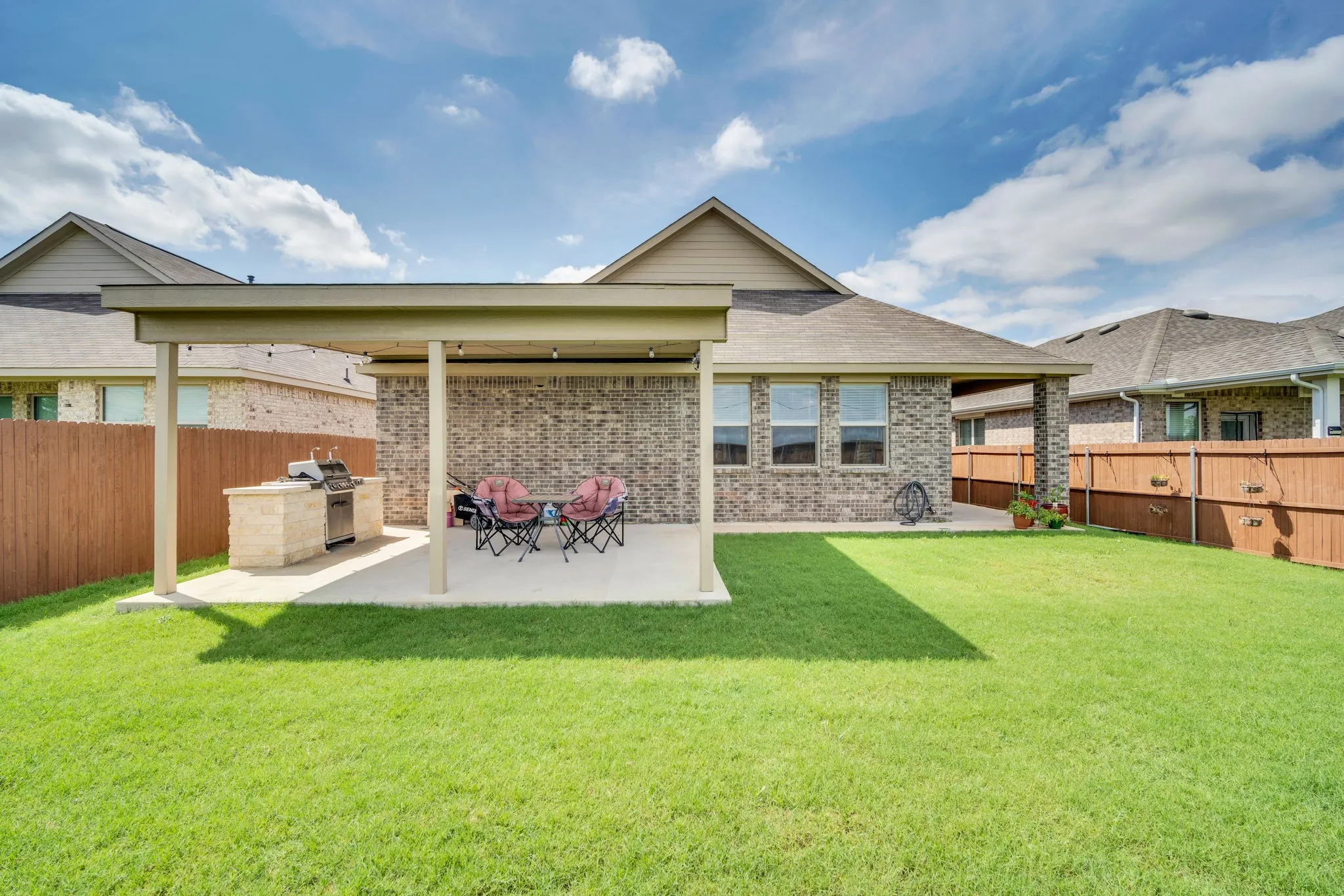 Expansive backyard featuring a covered patio, built-in outdoor grill station, concrete patio surface, and a privacy fence