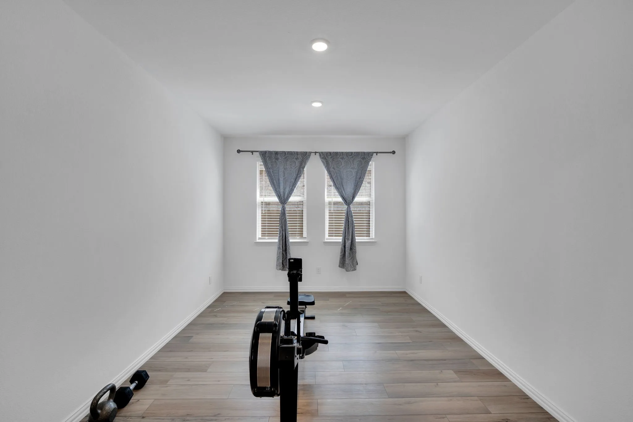 Room with wood-finish flooring, recessed lighting, and two windows featuring blinds and curtains