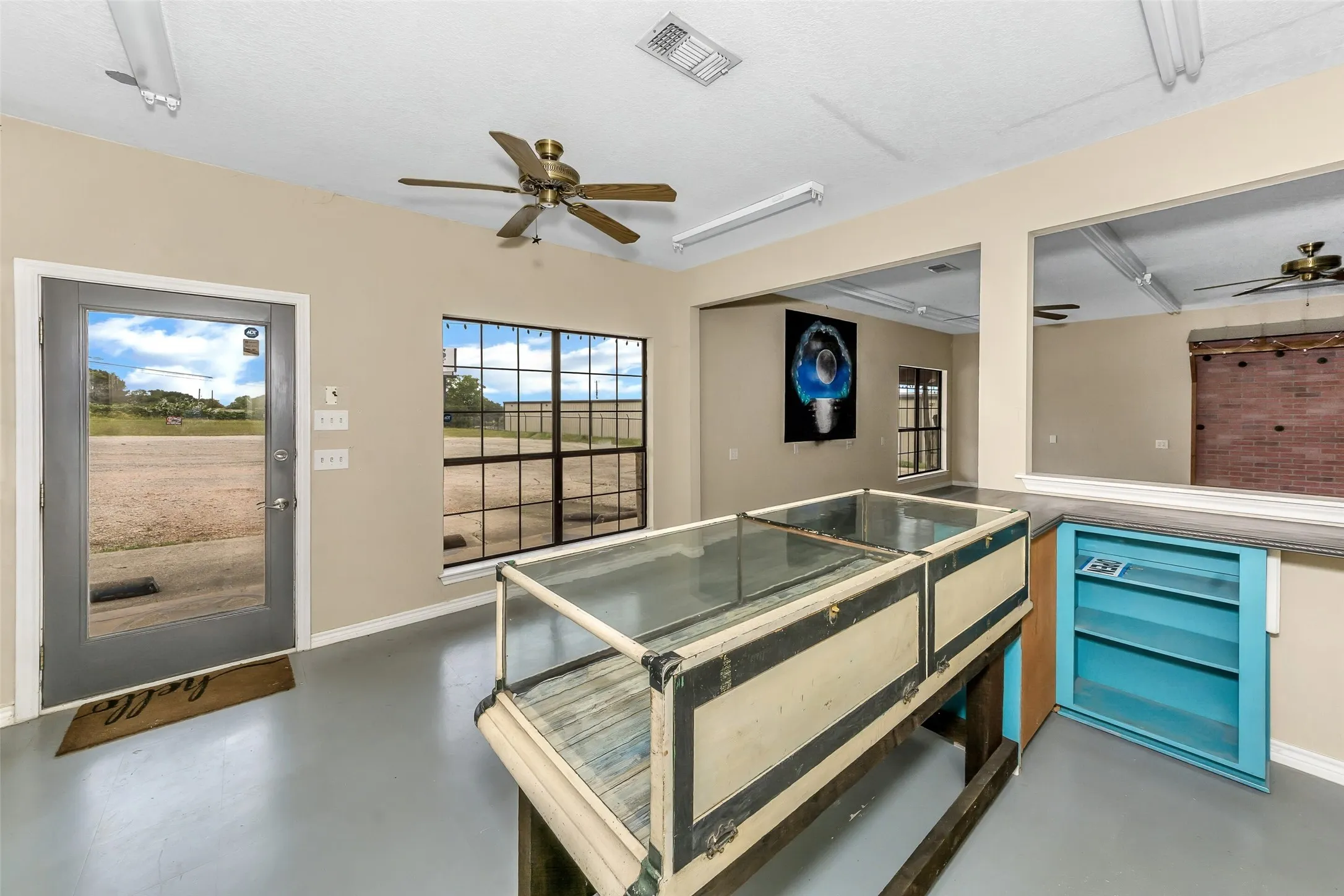 Open concept space featuring light gray flooring, large grid-pattern windows, a glass-paneled entry door, and a ceiling fan with integrated lighting