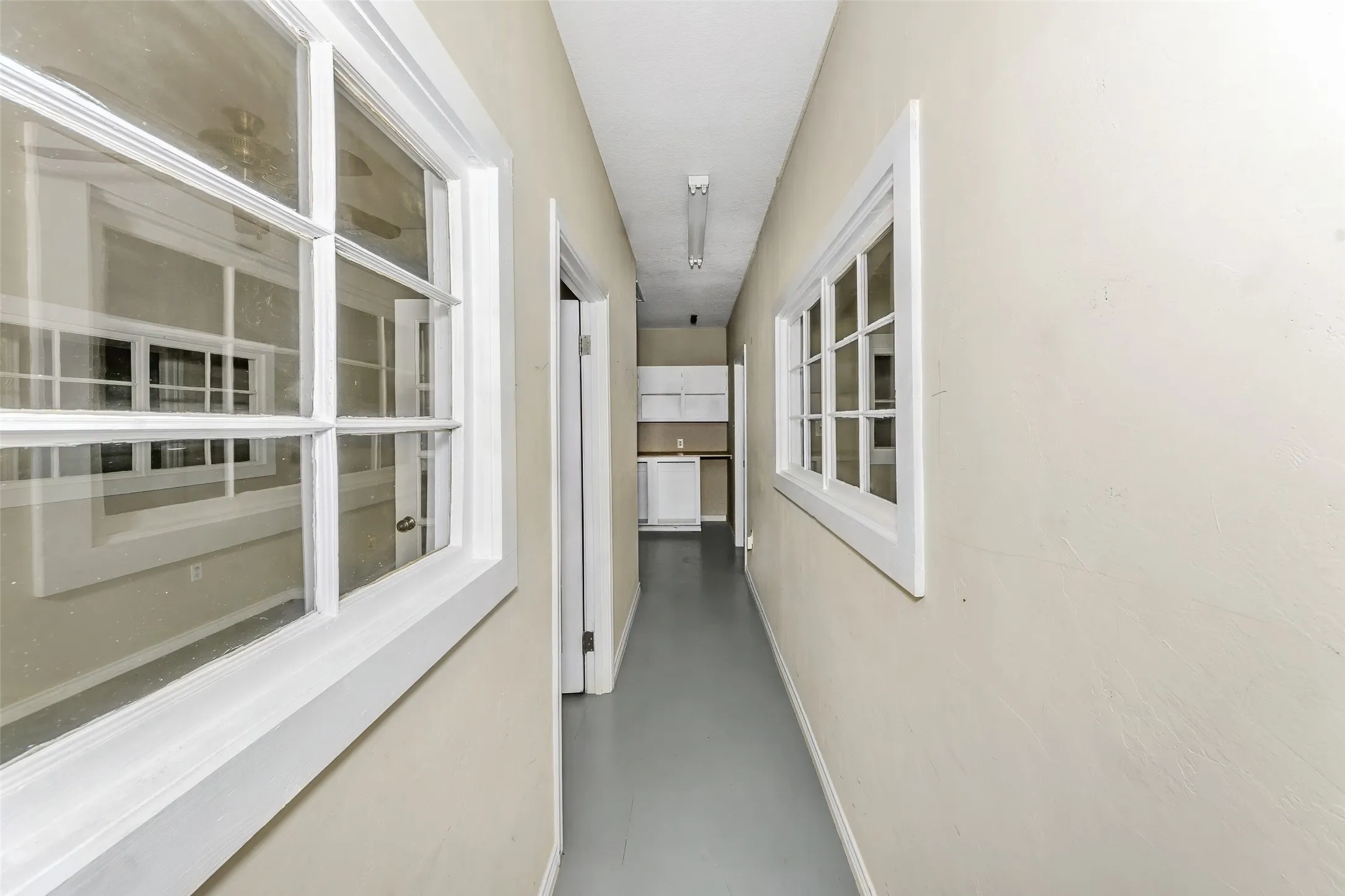 Hallway featuring multiple paned windows with white trim, light-toned walls, and grey flooring