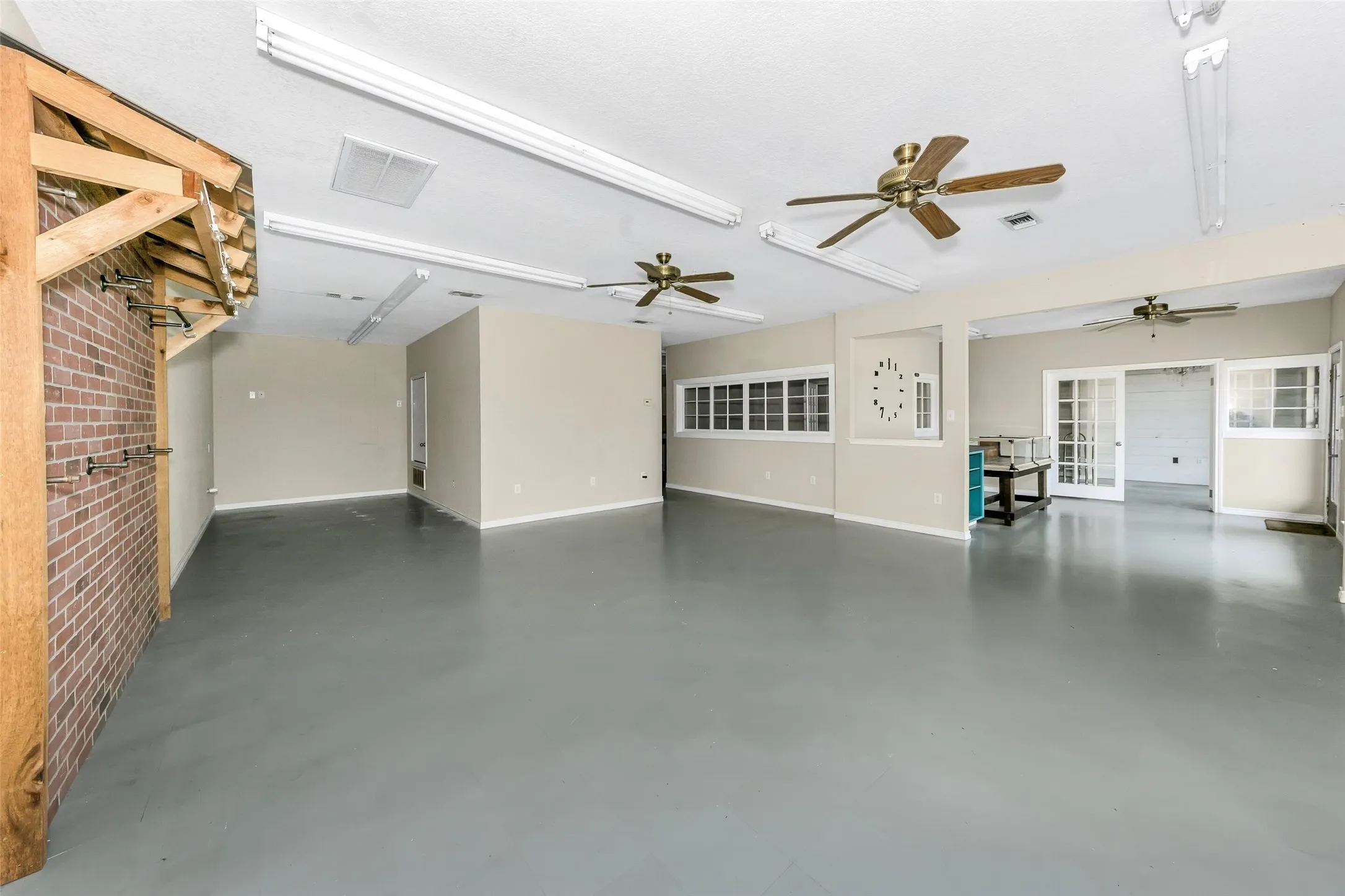Spacious interior featuring a gray concrete floor, exposed brick wall, multiple ceiling fans, recessed lighting, and French doors